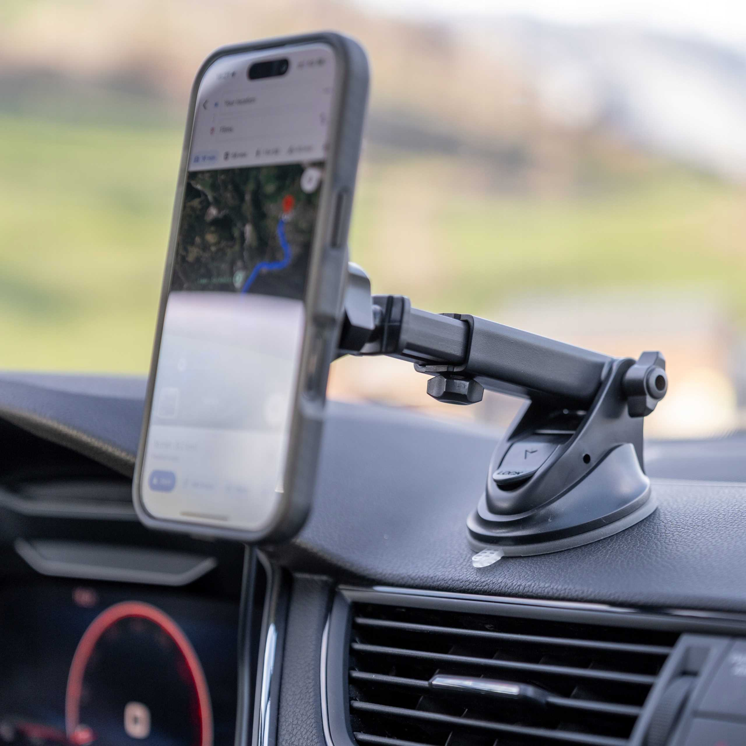 Telefon z mapą zamontowany na czarnym uchwycie samochodowym. Uchwyt jest przymocowany do deski rozdzielczej.