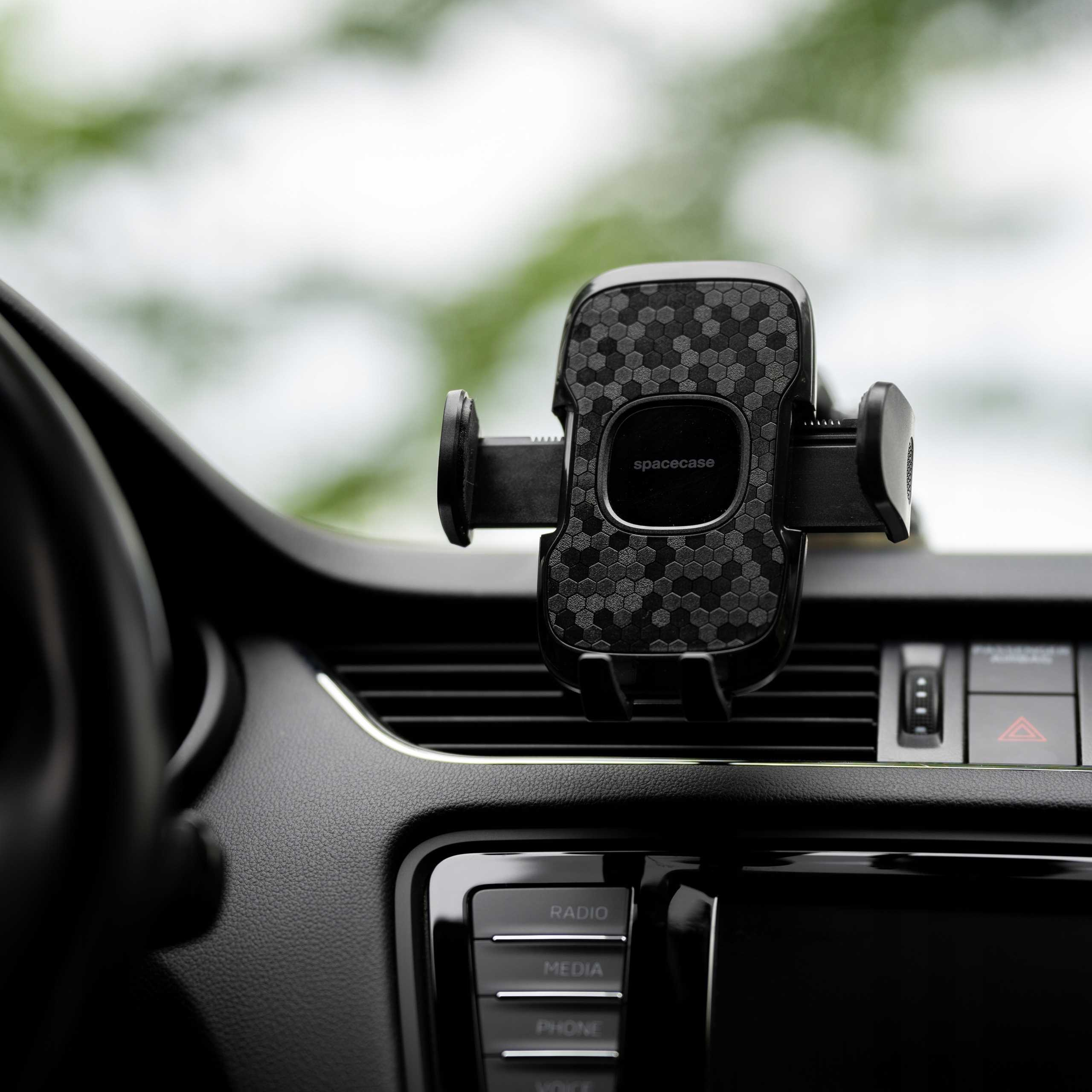 Wnętrze samochodu z uchwytem na telefon. Czarna deska rozdzielcza z przyciskami radia samochodowego i światłami awaryjnymi. Rozmyte zielone tło.