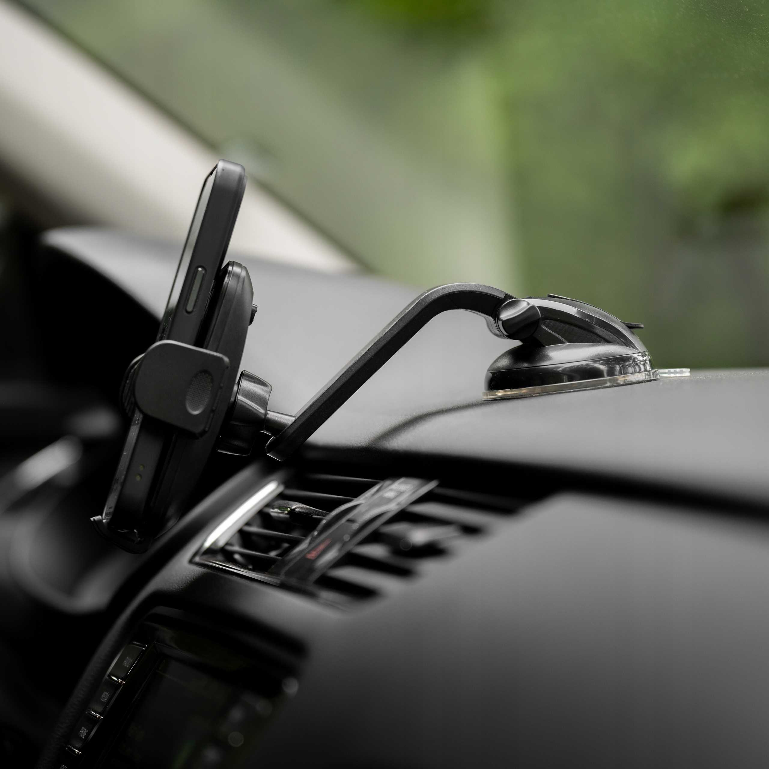 Czarny telefon w uchwycie samochodowym na desce rozdzielczej. Zielone, rozmyte tło.