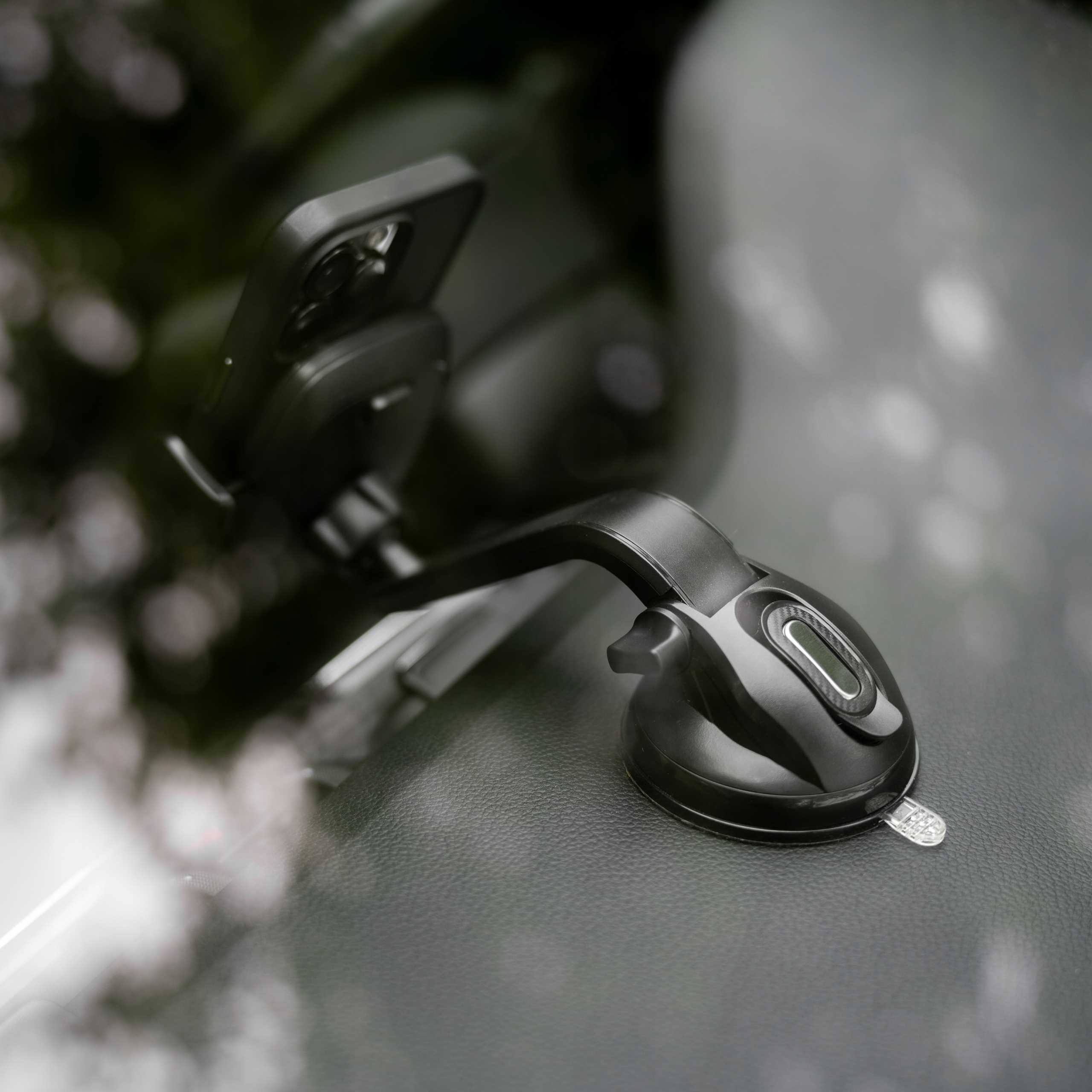 Czarny uchwyt na telefon jest zamontowany na przedniej szybie i trzyma telefon. Znajduje się na czarnej desce rozdzielczej.