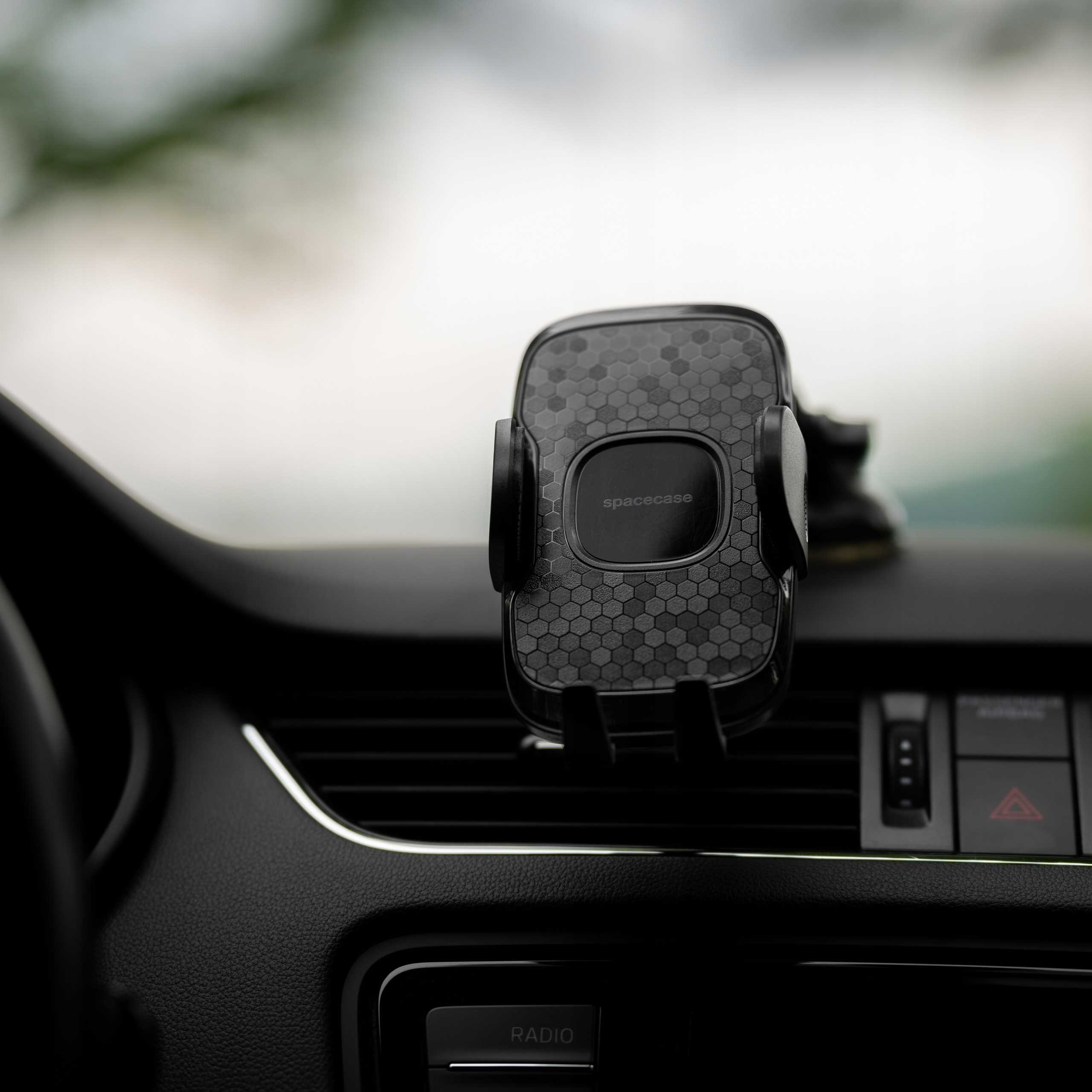 Wnętrze samochodu z czarnym uchwytem na telefon, z wzorem plastra miodu. Uchwyt jest zamontowany na desce rozdzielczej.