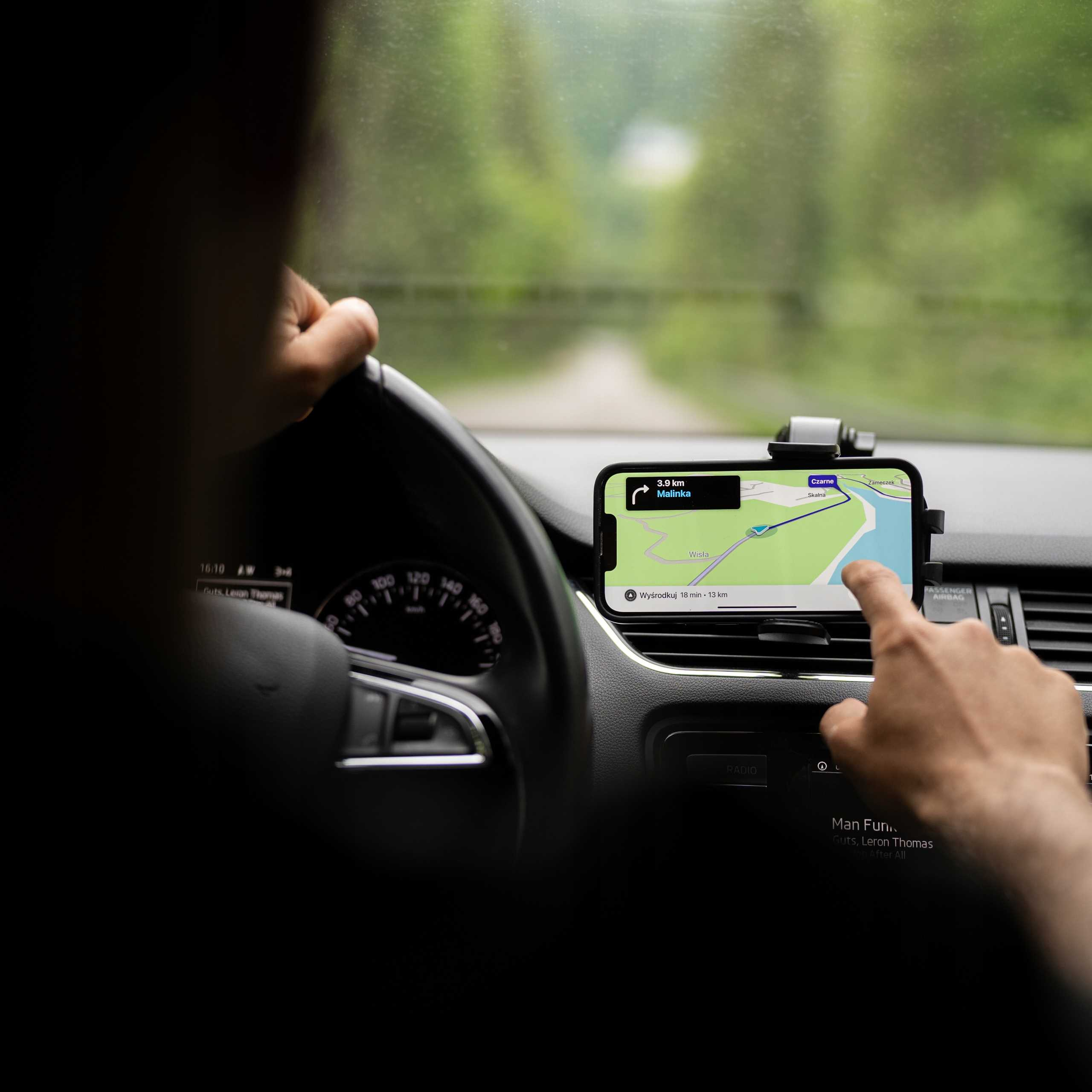 Osoba korzystająca z telefonu z aplikacją nawigacyjną w samochodzie, z rękami na kierownicy.