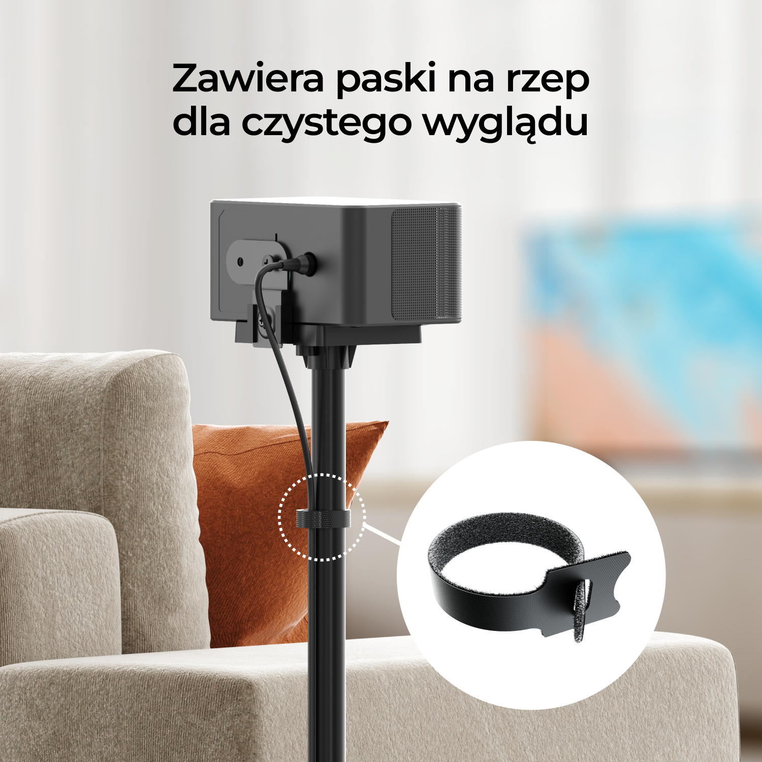 Czarny projektor jest zamontowany na statywie z kablem. Pasek na rzep jest pokazany w okręgu. W tle kanapa i pomarańczowa poduszka.