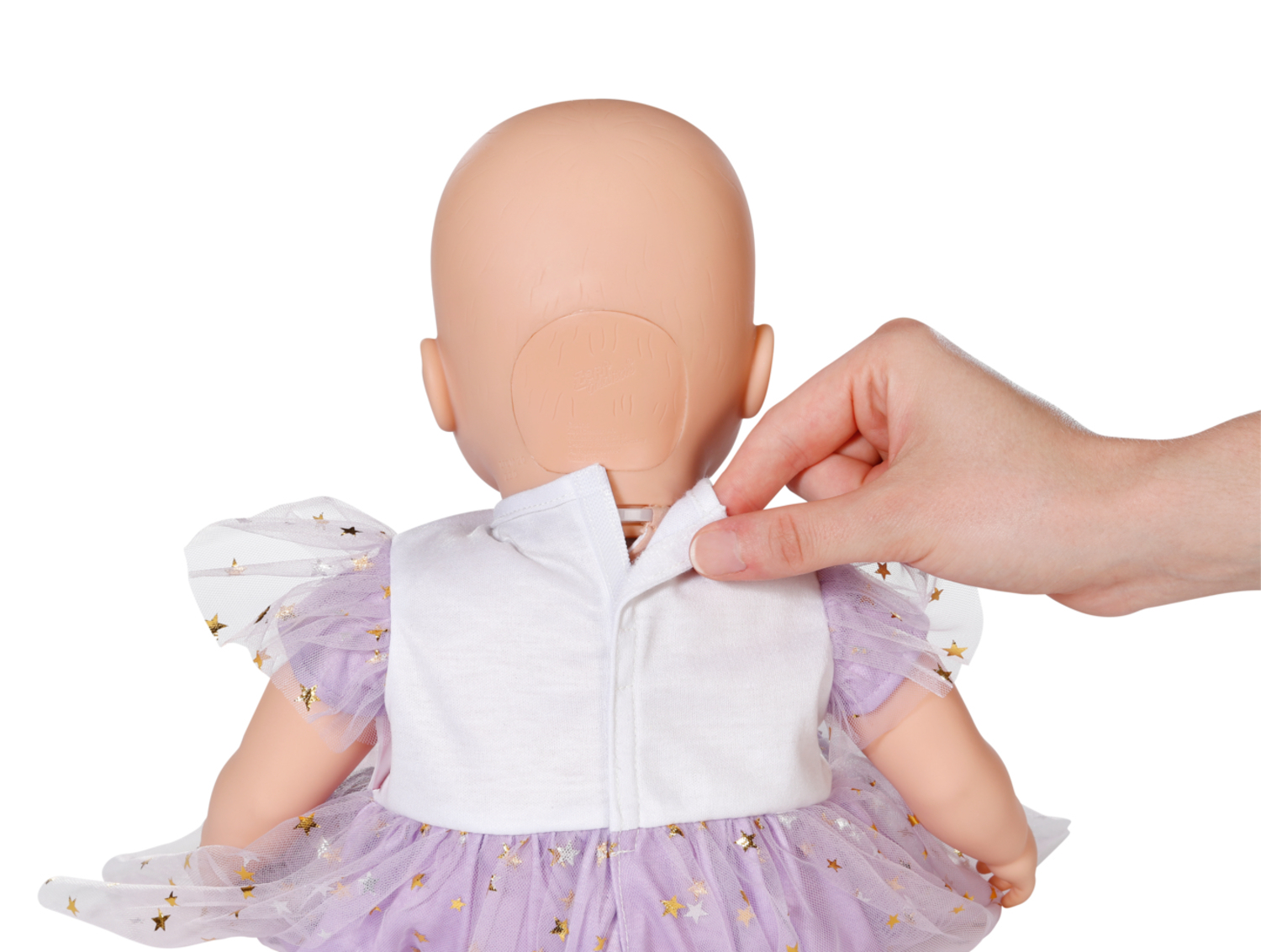 Una mano desabrocha la parte trasera de una camiseta blanca de muñeca. La muñeca lleva un vestido morado con estrellas doradas y tiene la cabeza calva.