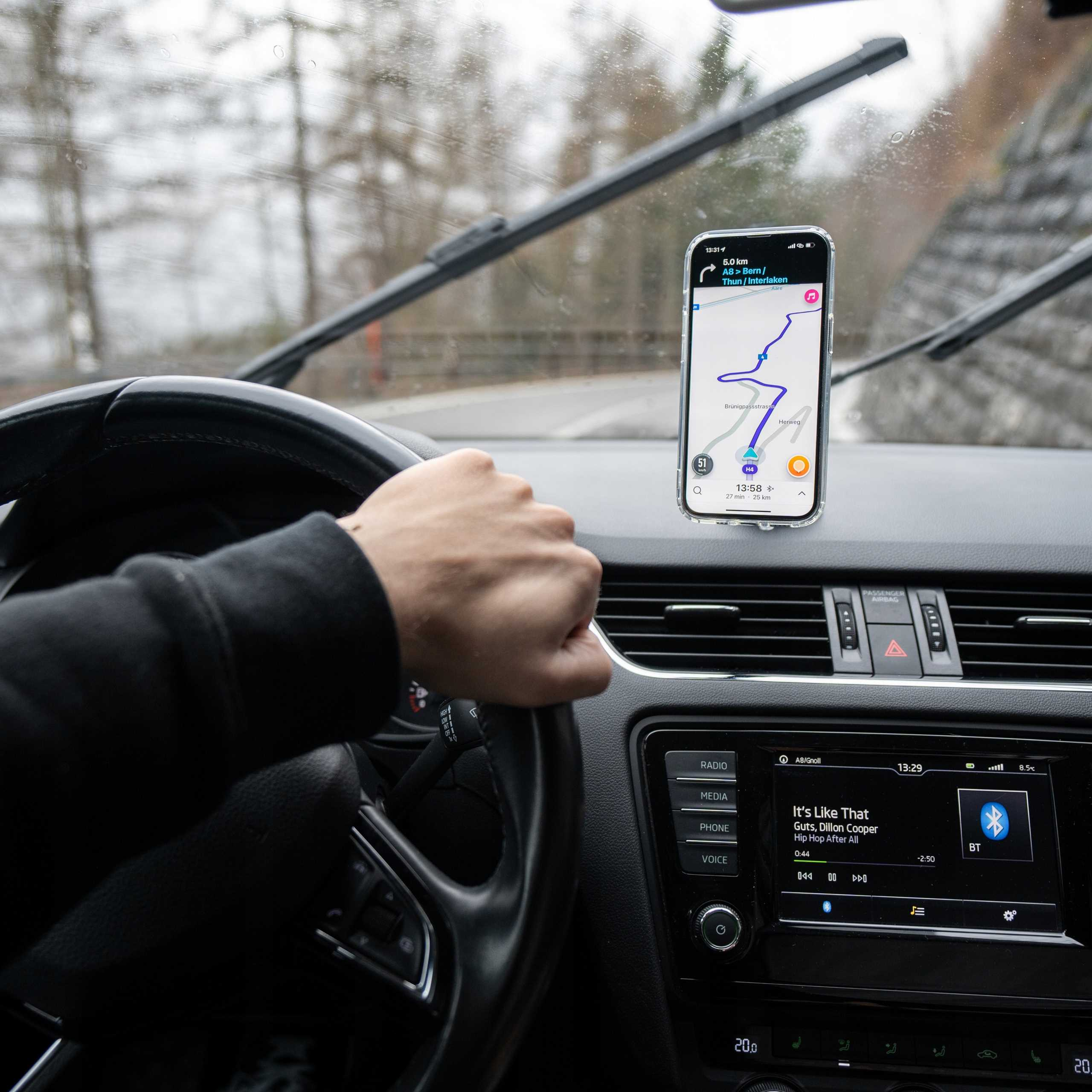 Wnętrze samochodu. Ręka na kierownicy. Telefon z mapą. Wycieraczki czyszczą przednią szybę.