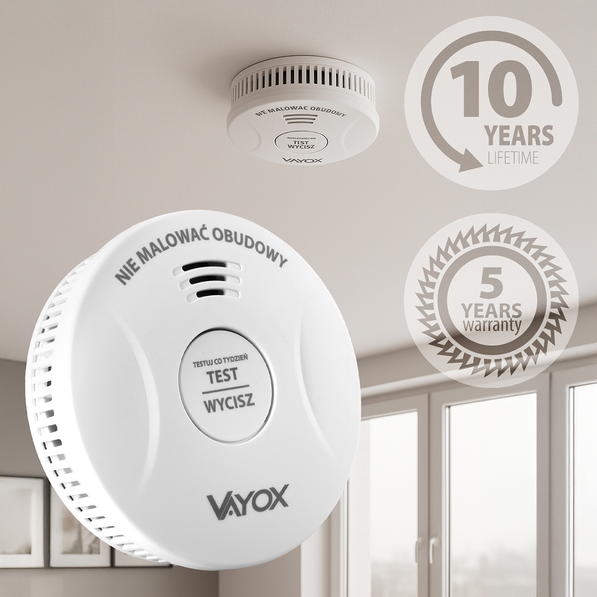 Biała czujka dymu Vayox zamontowana na suficie. Posiada przycisk testu i tekst w języku polskim. Grafiki wskazują 10 lat trwałości i 5 lat gwarancji.