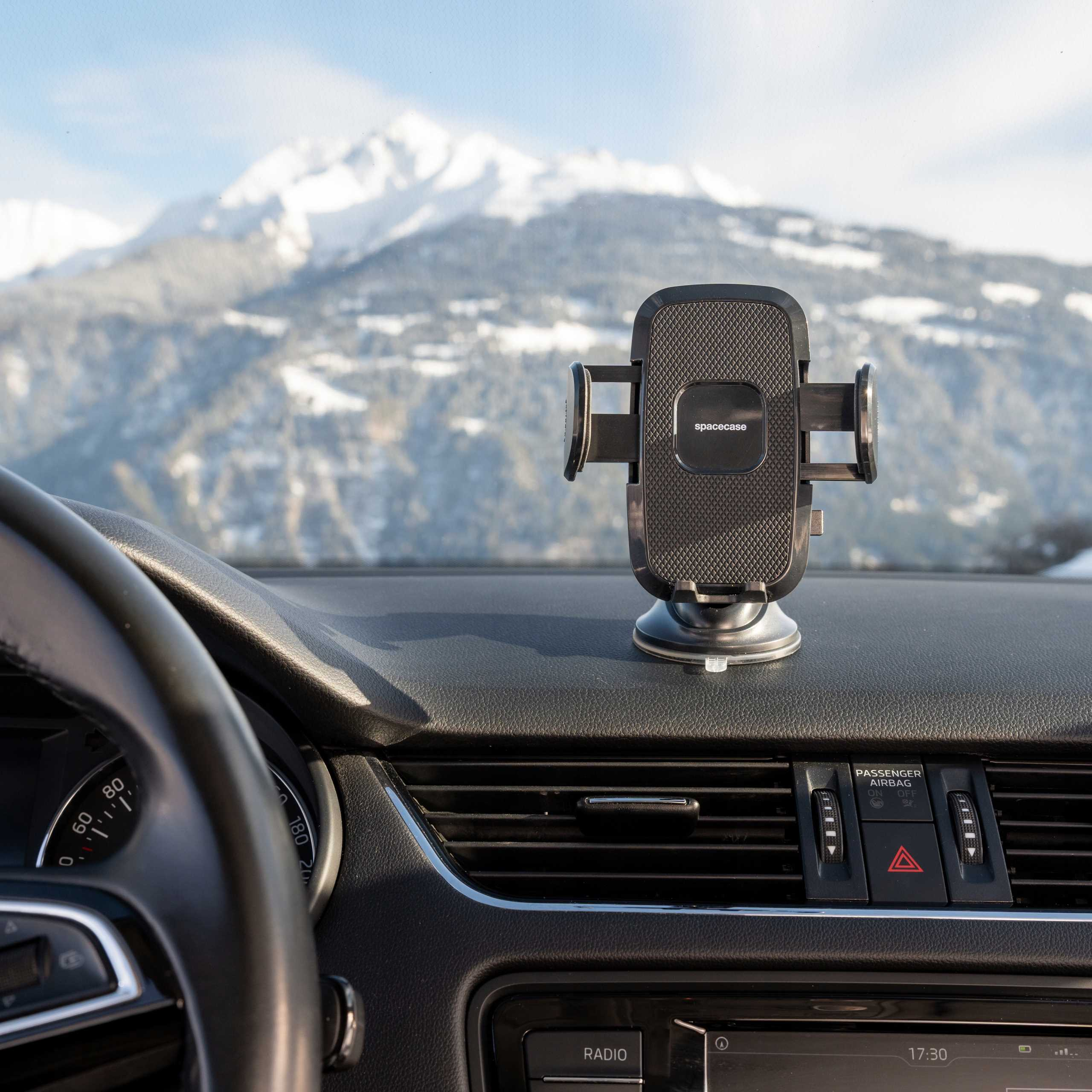 Wnętrze samochodu z uchwytem na telefon. Ośnieżone góry w tle. Kierownica na pierwszym planie.