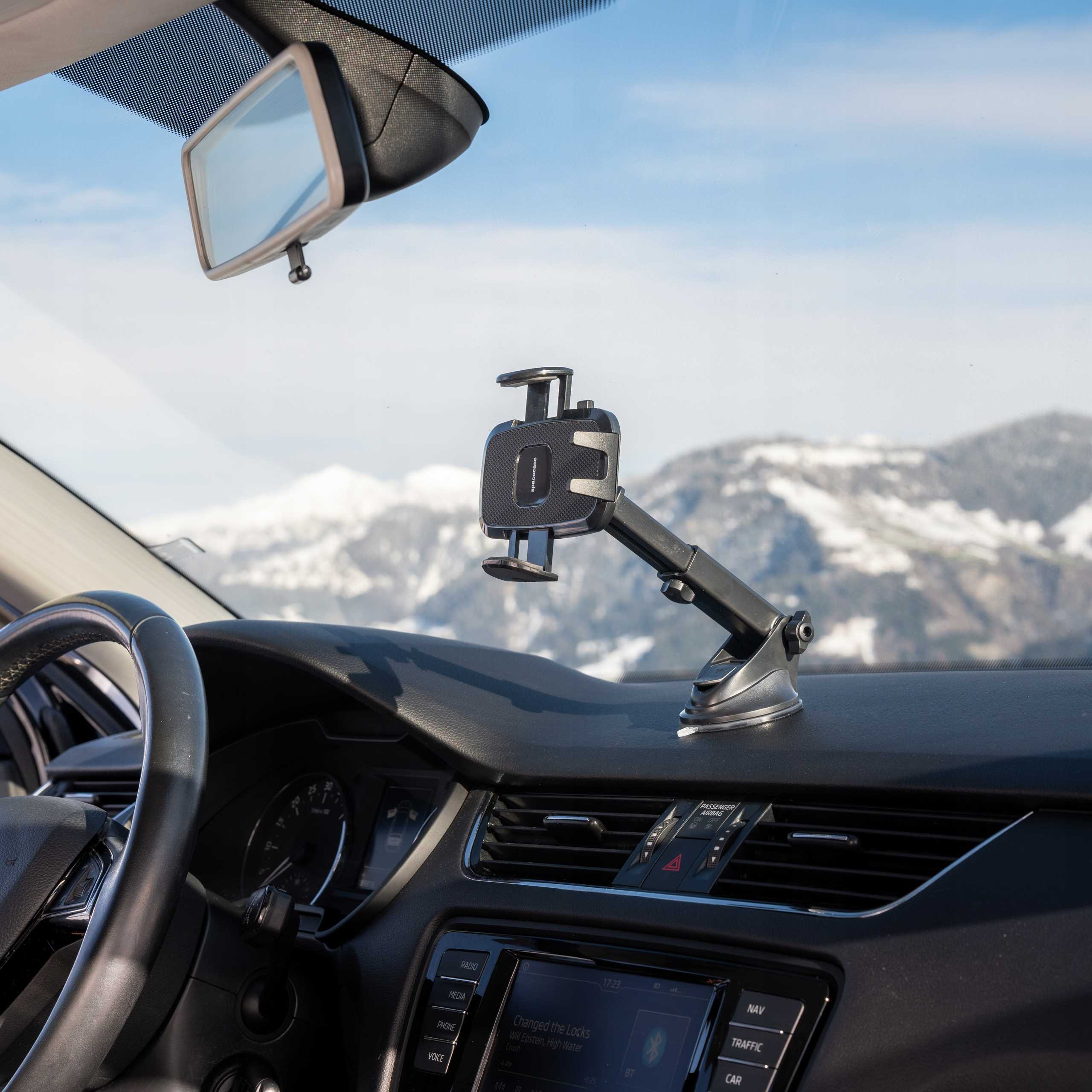 Widok wnętrza samochodu, uchwyt na telefon, kierownica, deska rozdzielcza, lusterko wsteczne, zaśnieżone góry w tle.