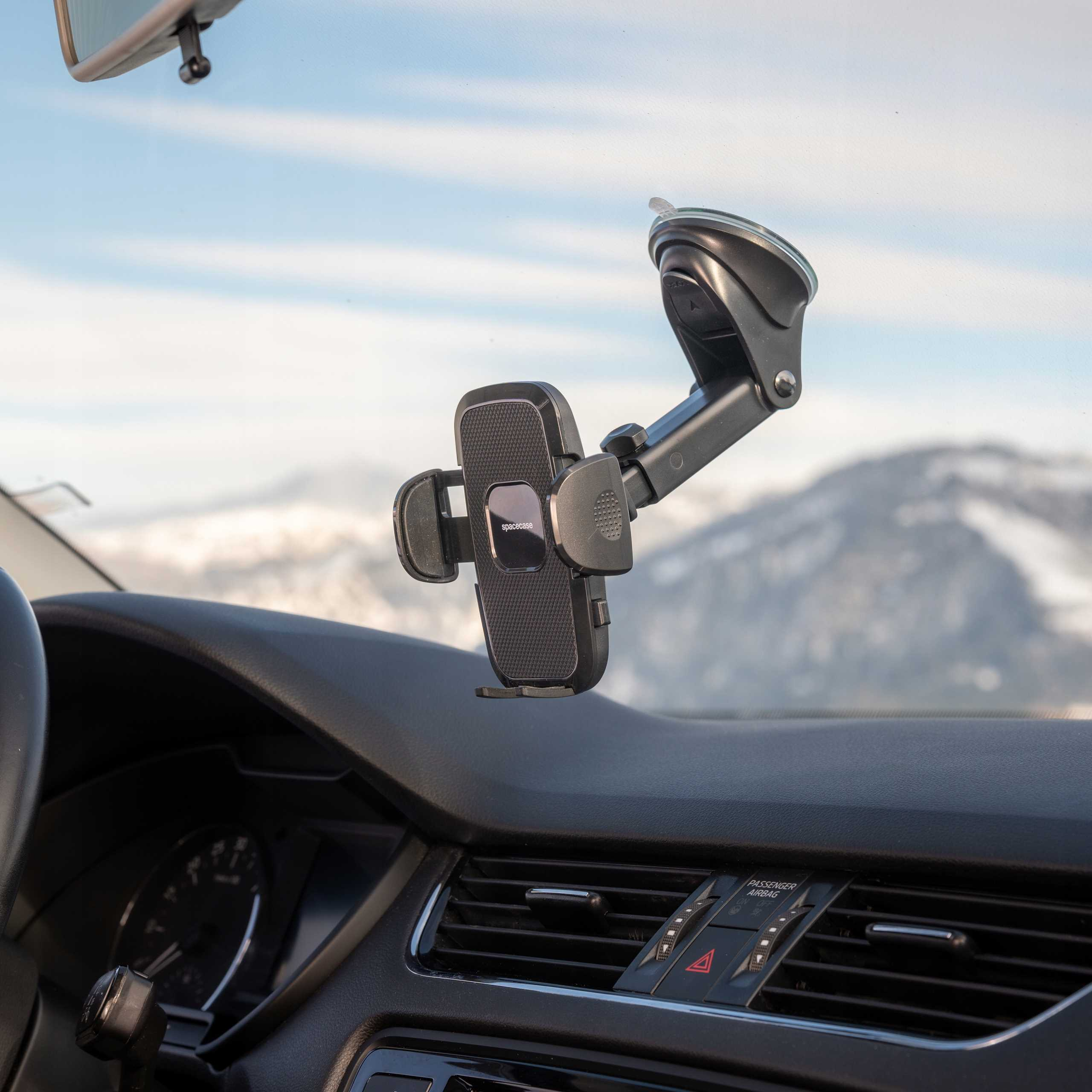 Wnętrze samochodu z uchwytem na telefon przymocowanym do przedniej szyby. W tle widoczny łańcuch górski.