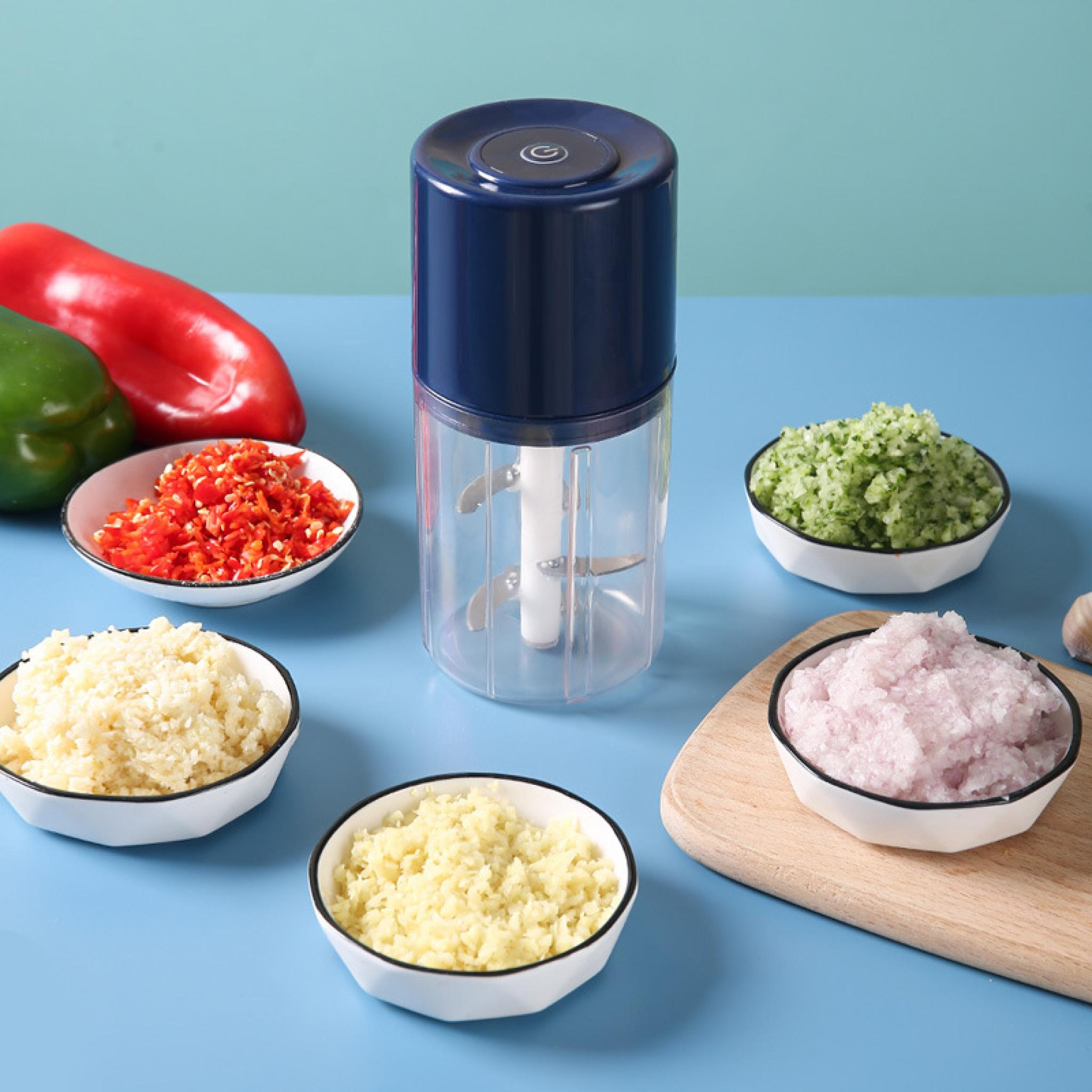 Ein Foodprocessor mit gehacktem Gemüse in Schüsseln. Paprika sind im Hintergrund. Blauer Untergrund.