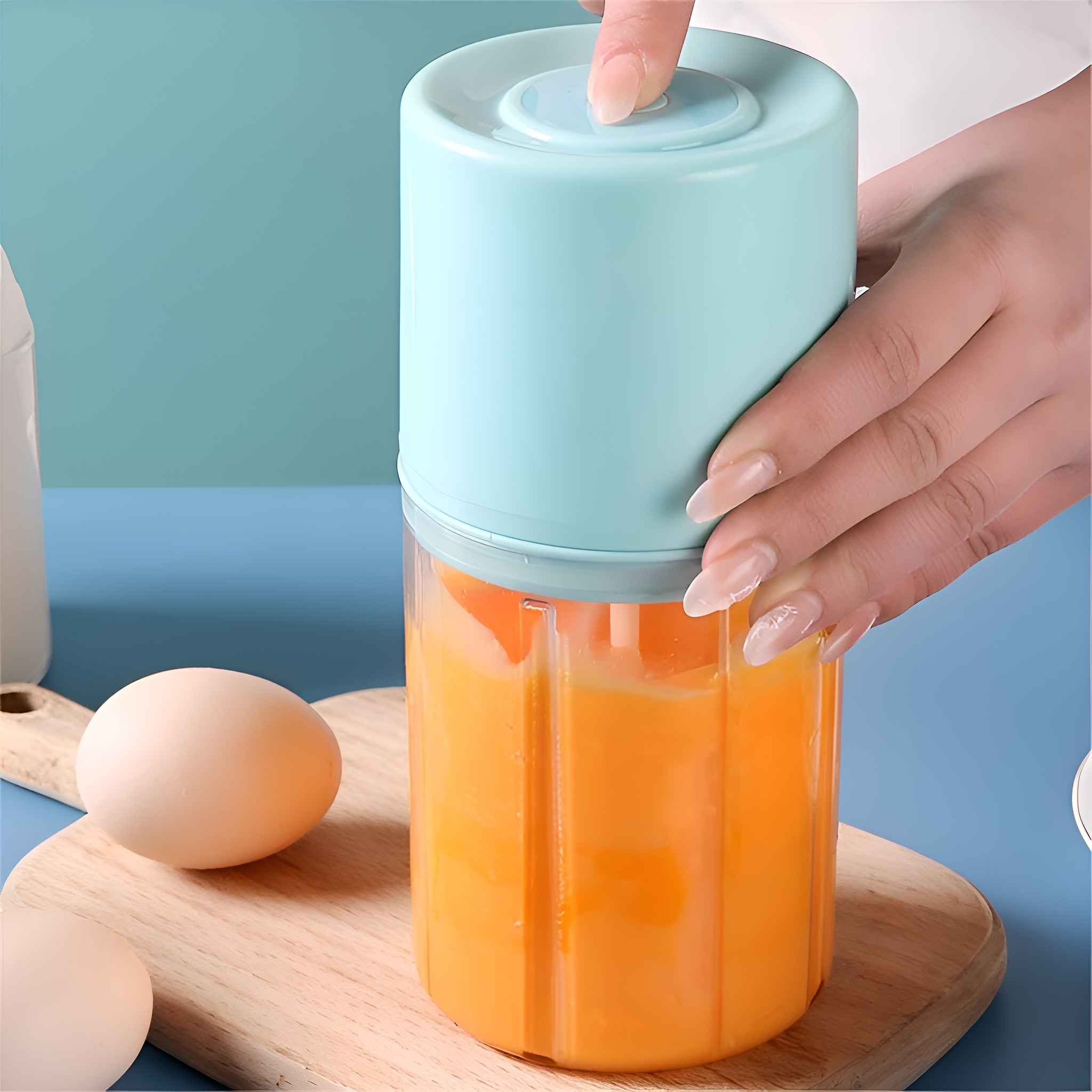 Eine Hand drückt einen Knopf auf einem blauen Mixer mit orangefarbener Flüssigkeit. Ein Ei liegt auf einem Holzbrett.