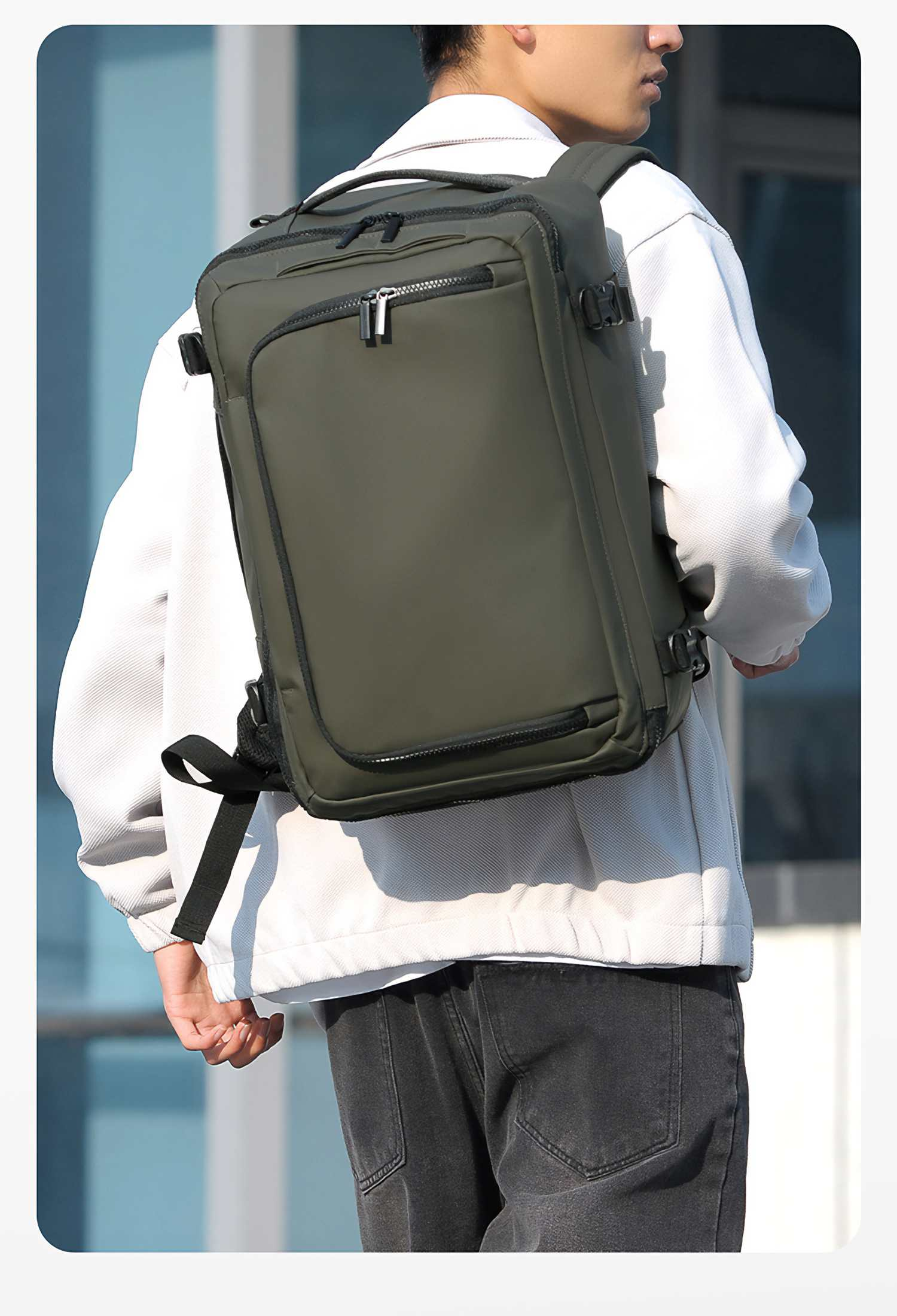 Eine Person mit weißer Jacke und schwarzer Jeans trägt einen grünen Rucksack. Im Hintergrund ist ein Gebäude zu sehen.
