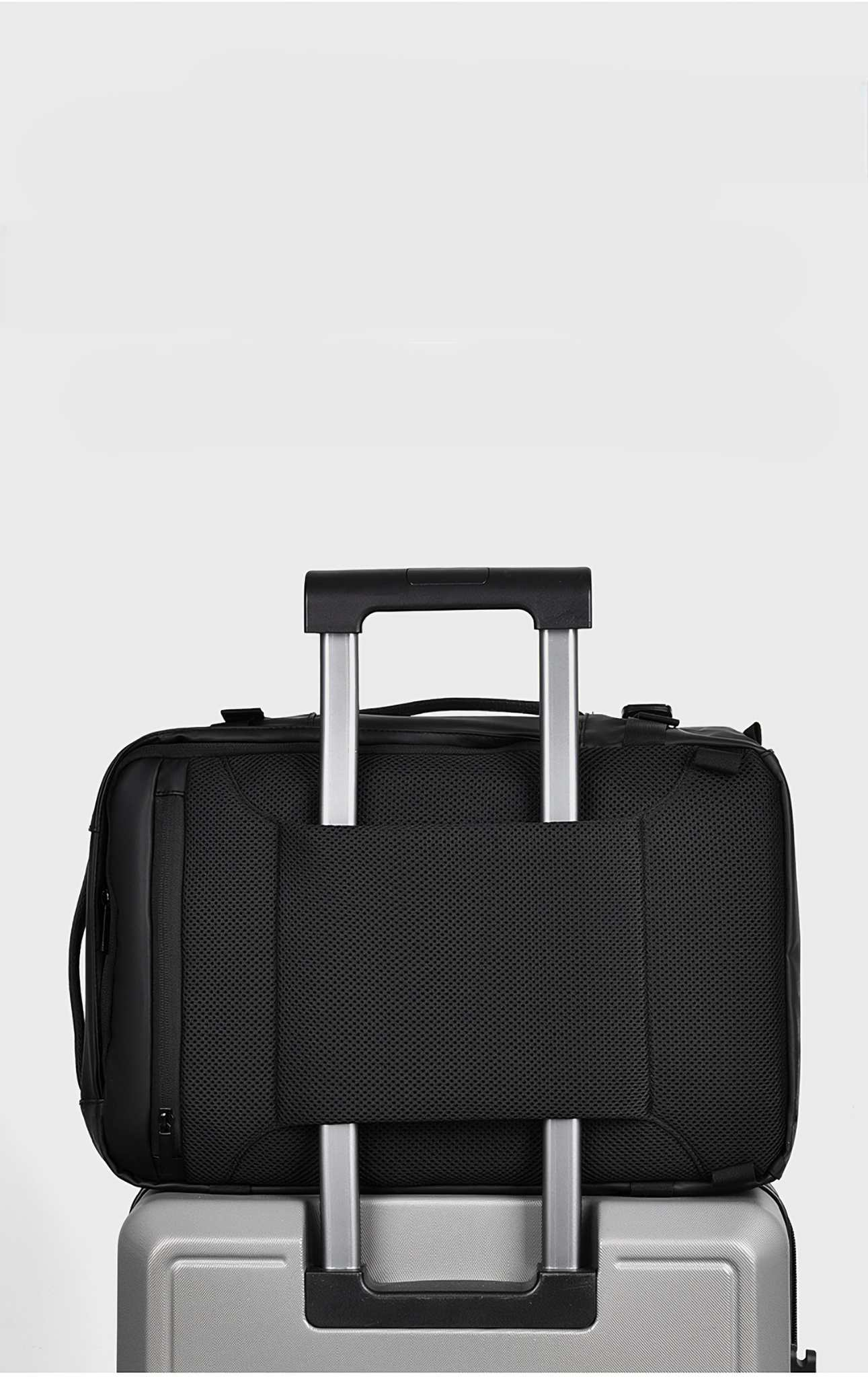 Schwarze Reisetasche auf einem silbernen Koffer. Die Tasche hat eine Netztasche und einen Griff. Weißer Hintergrund.