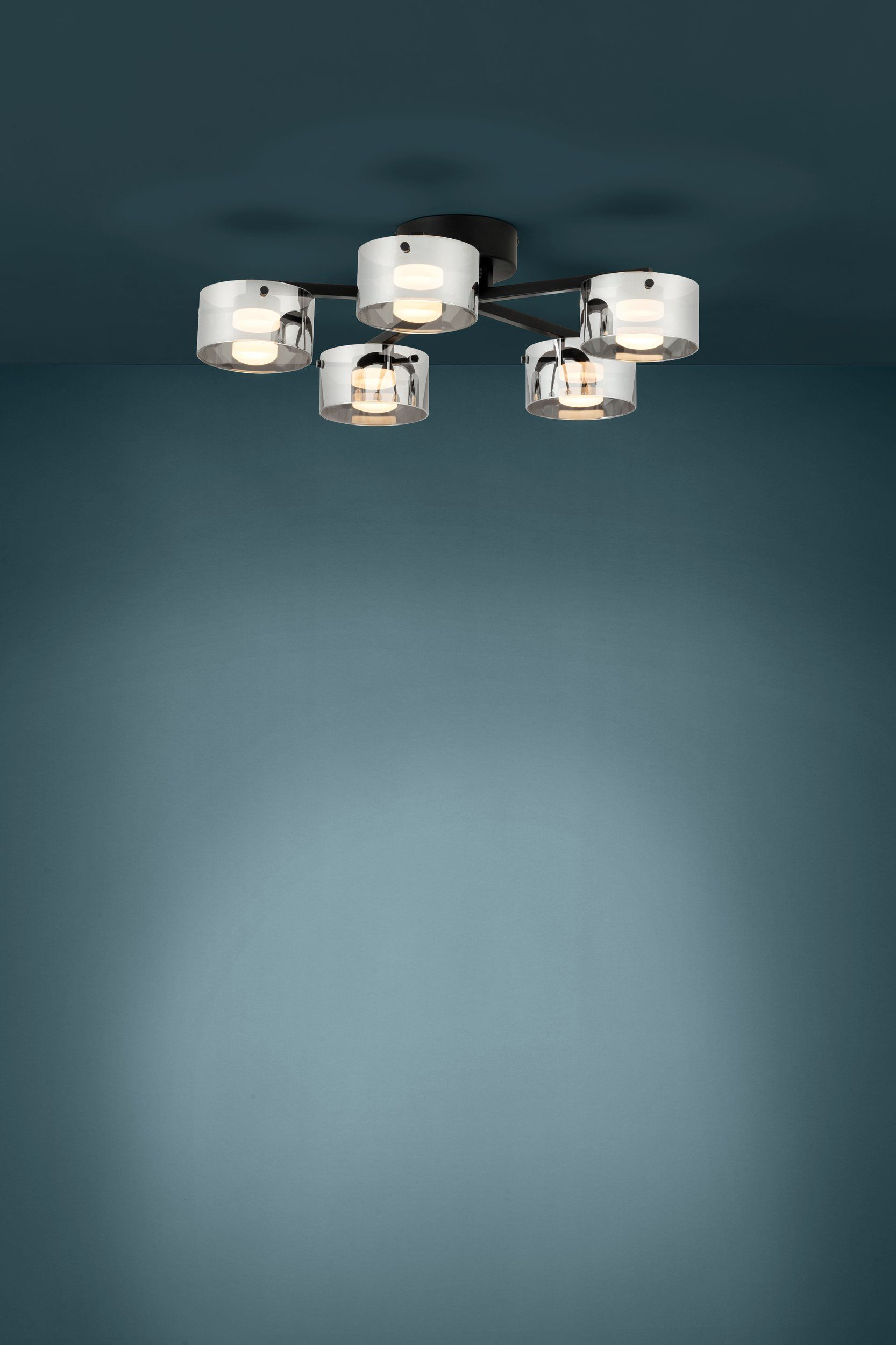Un plafonnier moderne avec six abat-jours en verre transparent, chacun avec une ampoule, sur fond turquoise.
