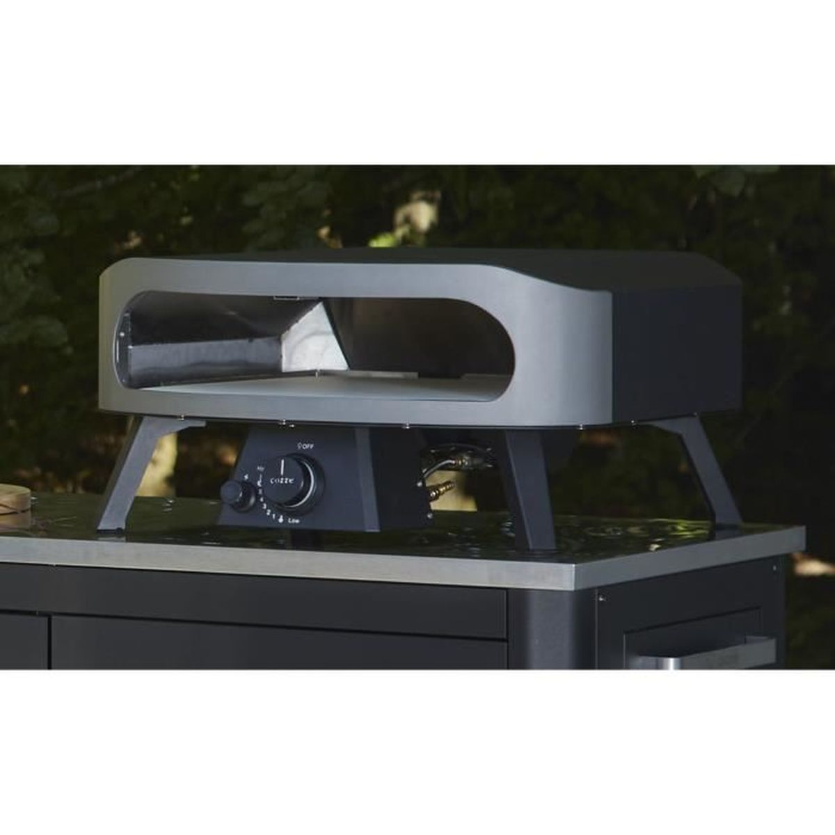 Ein schwarzer und silberner Pizzaofen steht auf einem schwarzen Tisch. Der Ofen hat eine gewölbte Oberseite und eine Frontöffnung. Der Hintergrund ist grün.