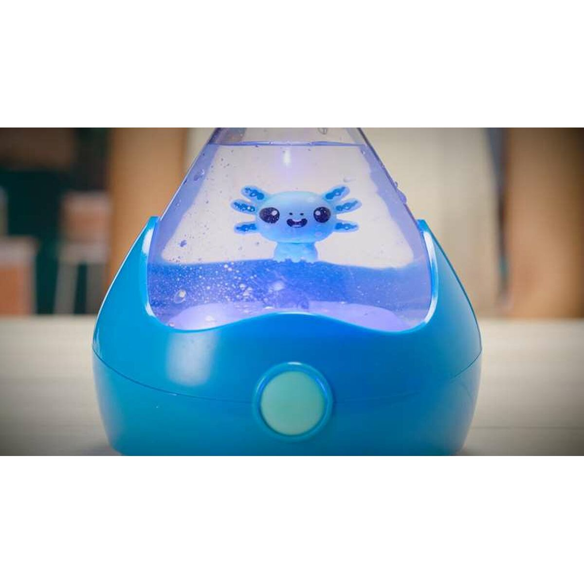 Un juguete de ajolote azul dentro de un recipiente azul lleno de agua con un botón en la parte inferior. El juguete está iluminado.
