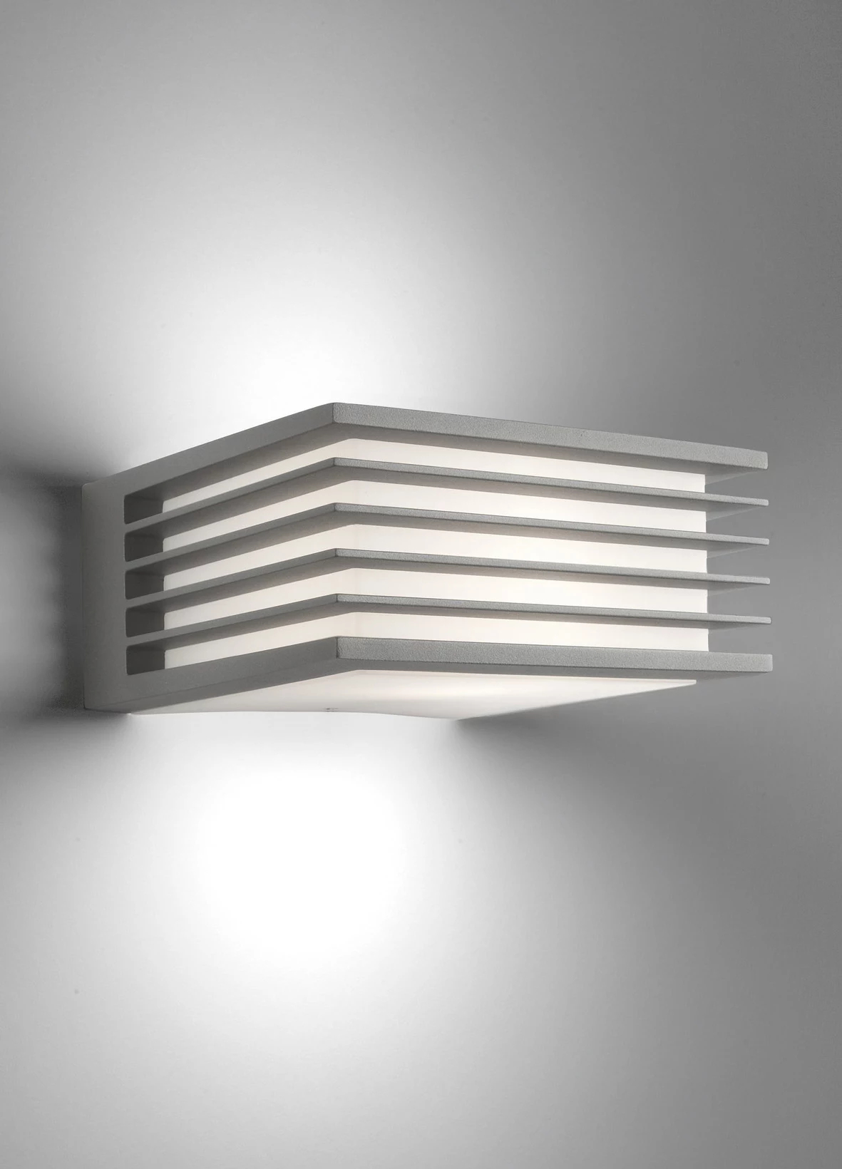 Eine rechteckige, geschichtete Wandleuchte ist an einer grauen Wand montiert. Sie hat horizontale, graue, rechteckige Platten.