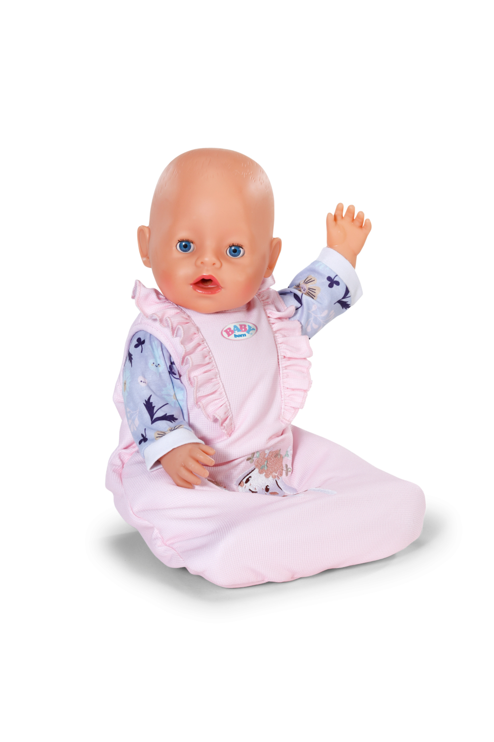 Lalka siedzi i macha ręką. Ma na sobie różowy strój z niebieskimi kwiatowymi rękawami. Lalka ma niebieskie oczy i łysą głowę.