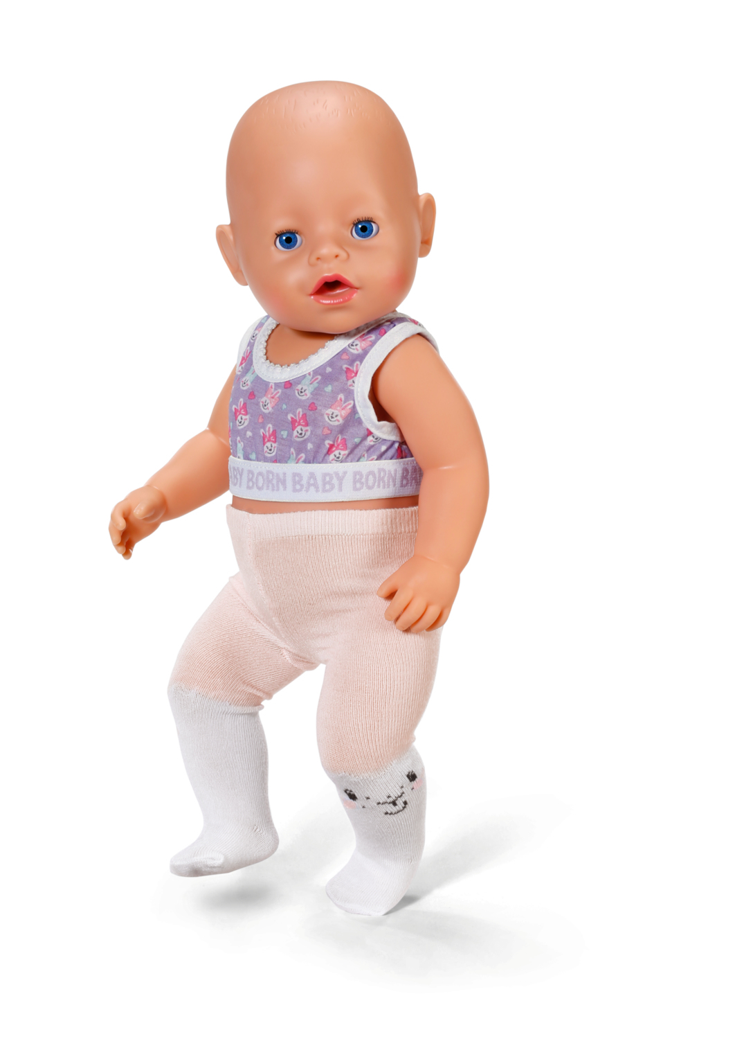 Lalka z niebieskimi oczami, ubrana w fioletową górę, różowe spodnie i białe skarpetki. Lalka stoi na białym tle.