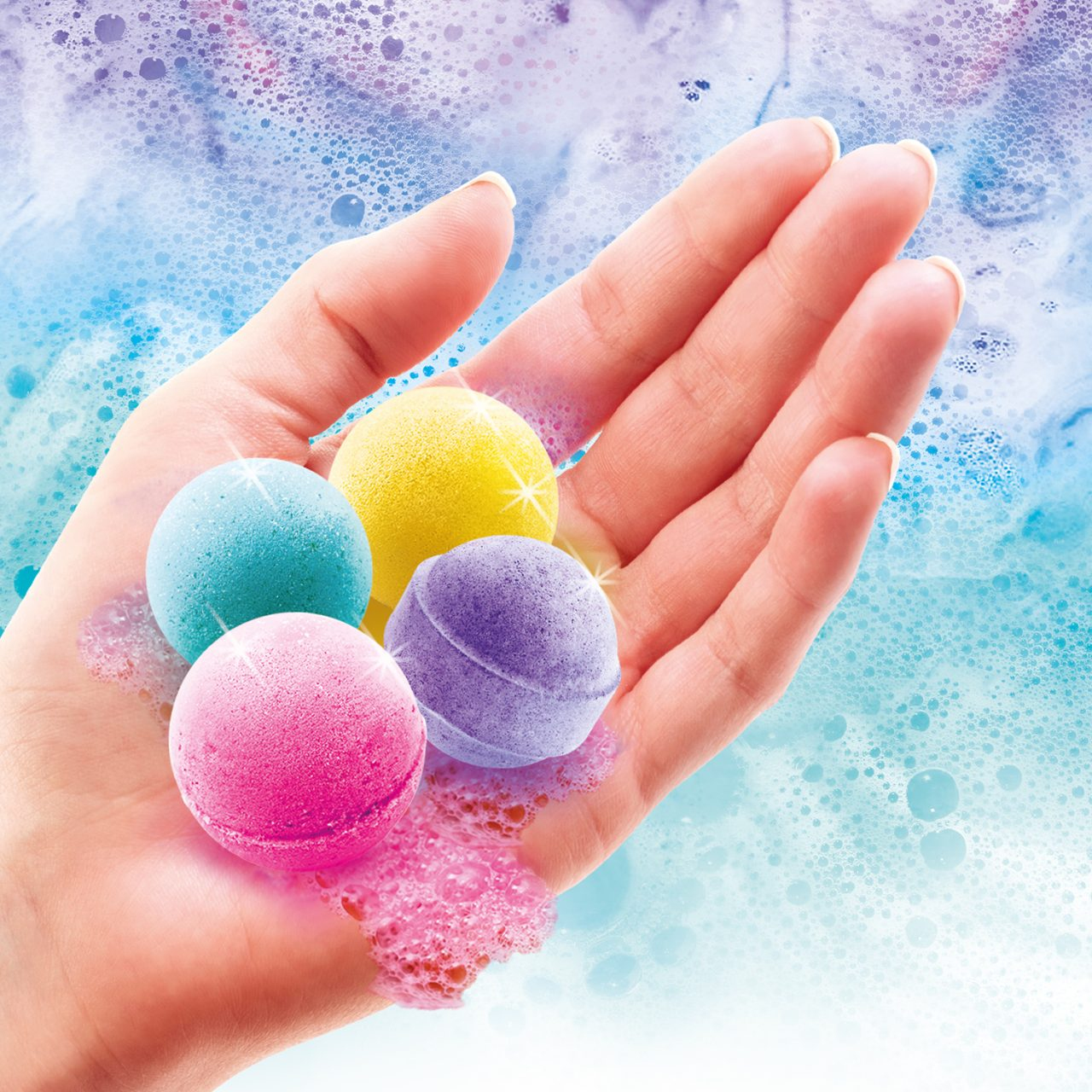 Dłoń trzyma cztery kolorowe kule do kąpieli. Różowe, niebieskie, żółte i fioletowe. Bąbelki otaczają dłoń na niebiesko-białym tle.