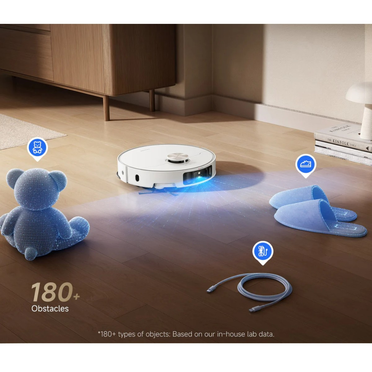 Ein Roboter-Staubsauger scannt einen Raum mit Hindernissen wie einem Teddybären, Hausschuhen und einem Kabel auf dem Holzboden.