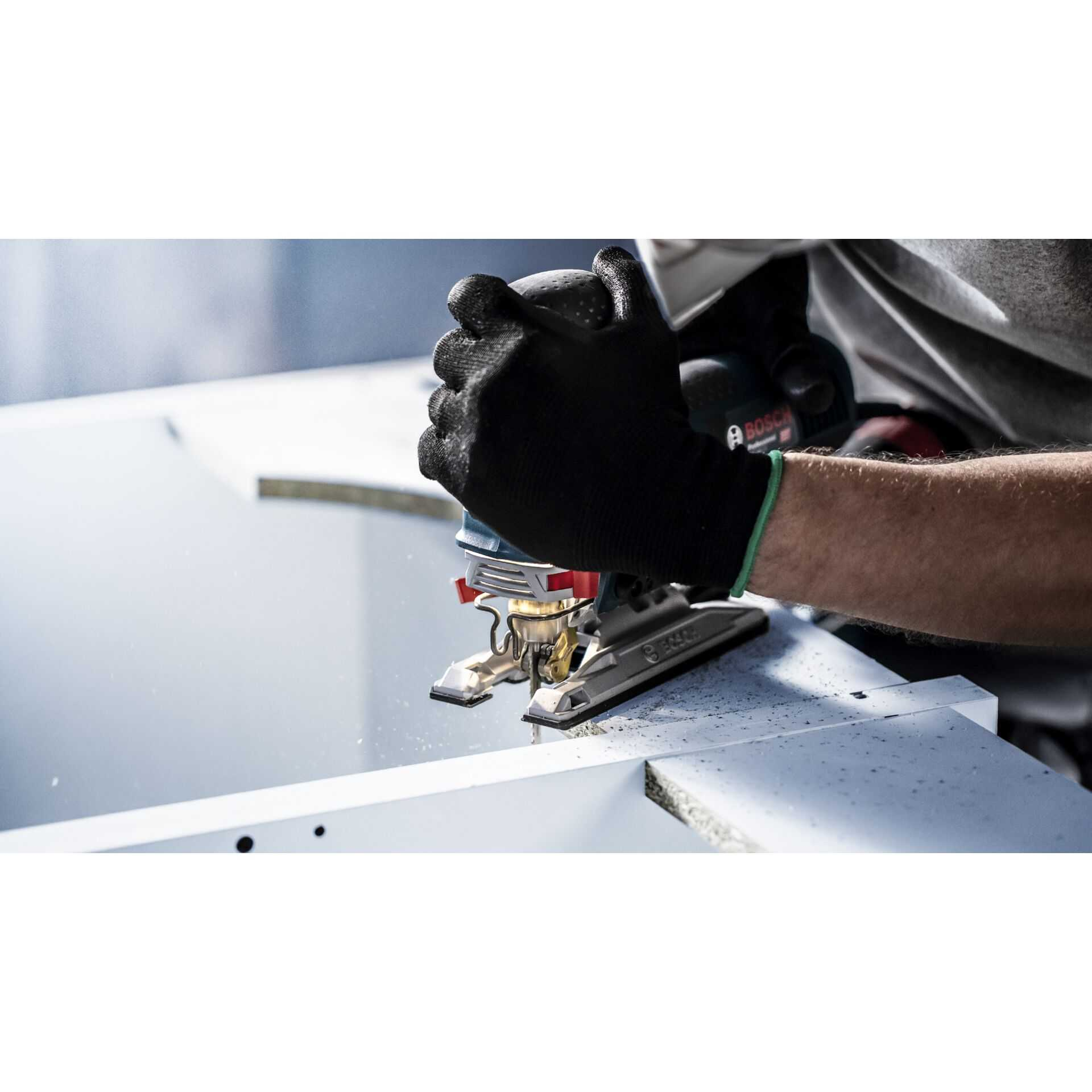 Osoba używa wyrzynarki do cięcia białej powierzchni. Ma na sobie czarną rękawicę. Narzędzie to Bosch.