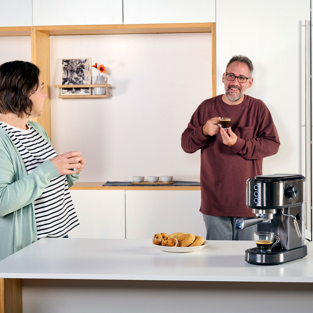 Mężczyzna i kobieta w kuchni z ekspresem do kawy. Mężczyzna trzyma filiżankę kawy, a kobieta również trzyma filiżankę.