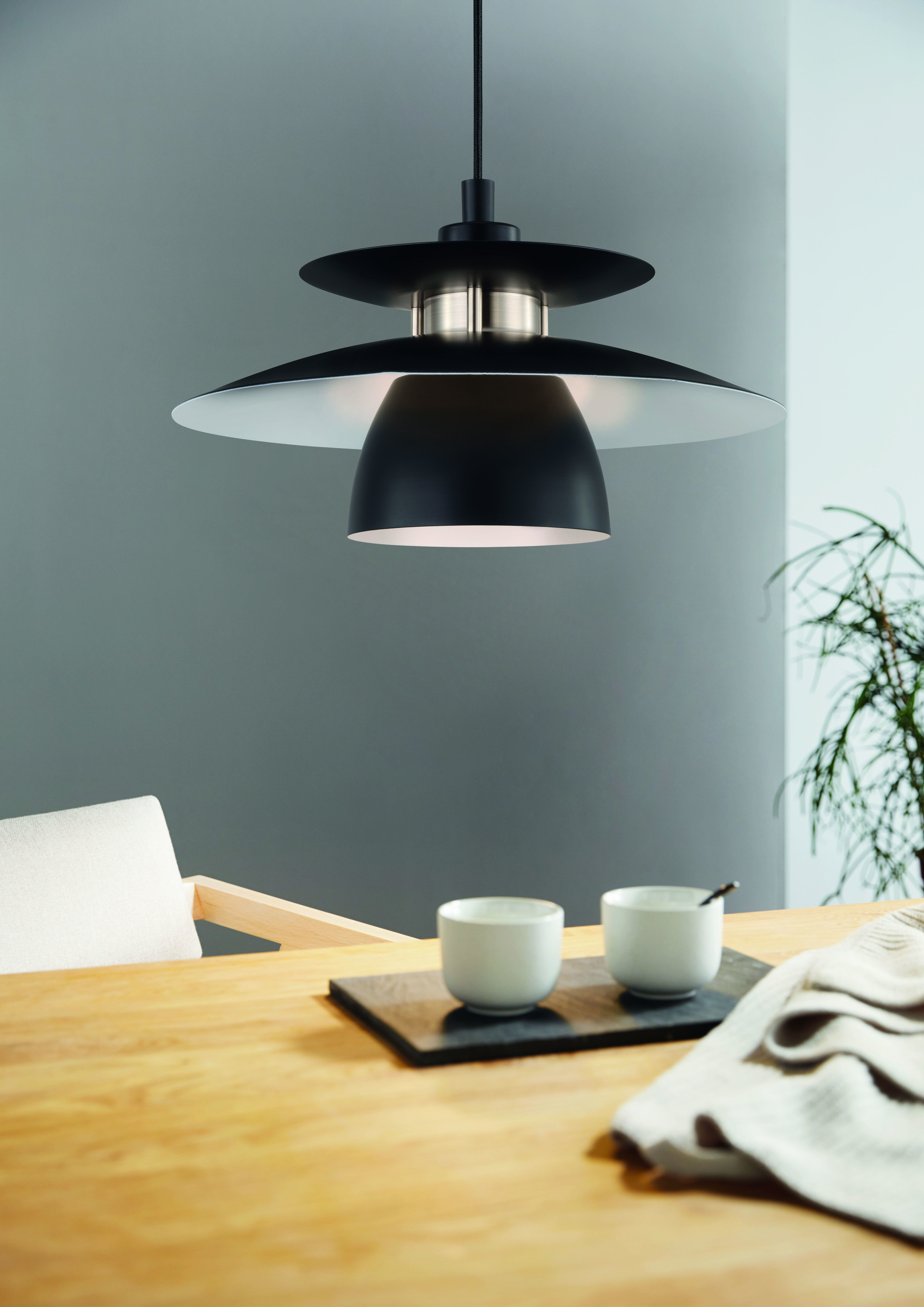 Eine moderne schwarze Lampe hängt über einem Holztisch mit zwei weißen Tassen auf einem dunklen Tablett.