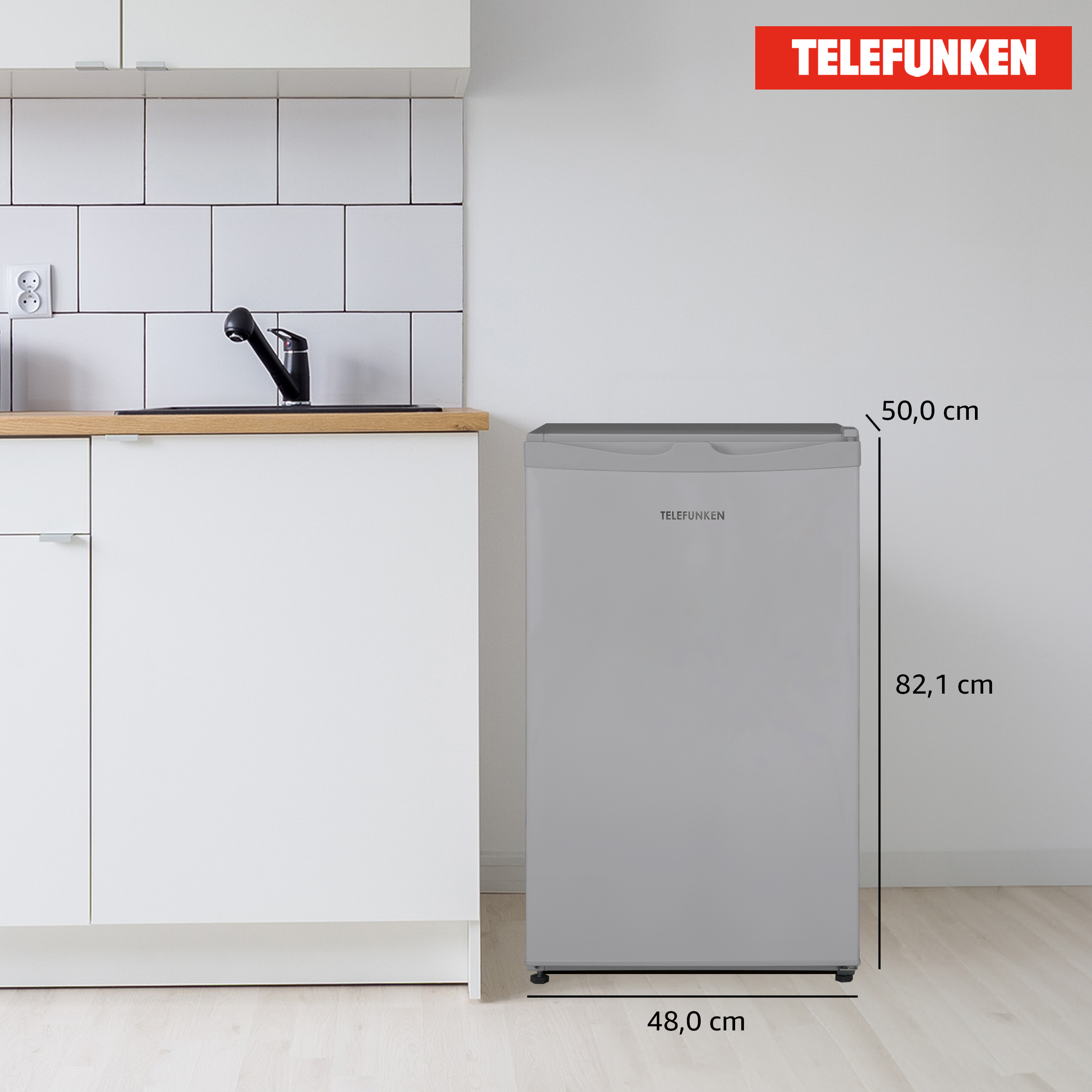 Ein grauer Telefunken-Kühlschrank steht in einer Küche. Er hat markierte Abmessungen. Weiße Schränke und eine geflieste Wand sind im Hintergrund.