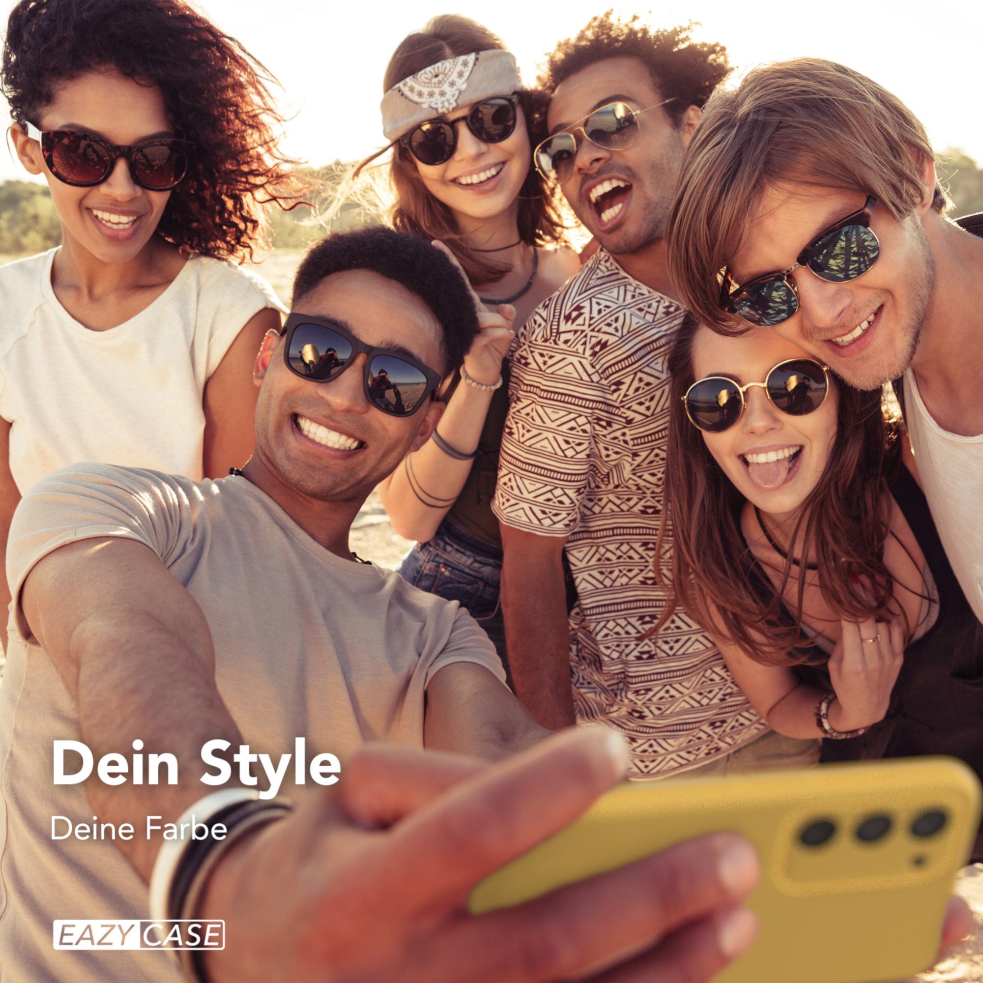 Eine Gruppe von sechs Personen macht an einem sonnigen Tag ein Selfie, alle lächeln und tragen Sonnenbrillen. Ein gelbes Telefon ist im Vordergrund.