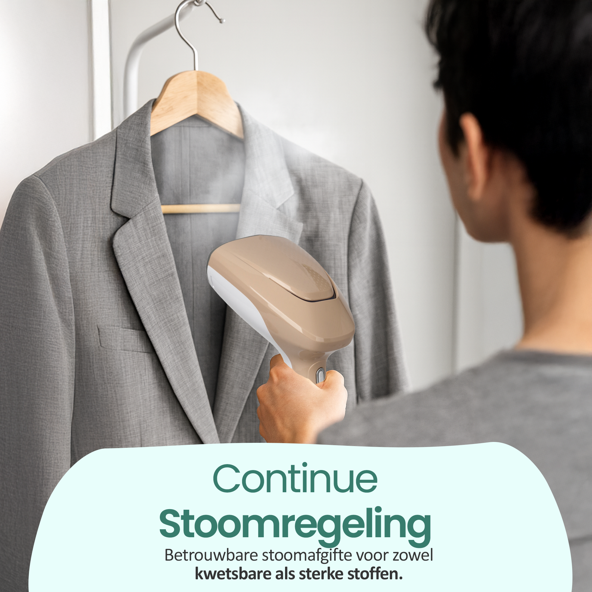 Een persoon stoomt een grijze blazer met een beige en witte steamer. De blazer hangt aan een houten hanger. De achtergrond is onscherp.