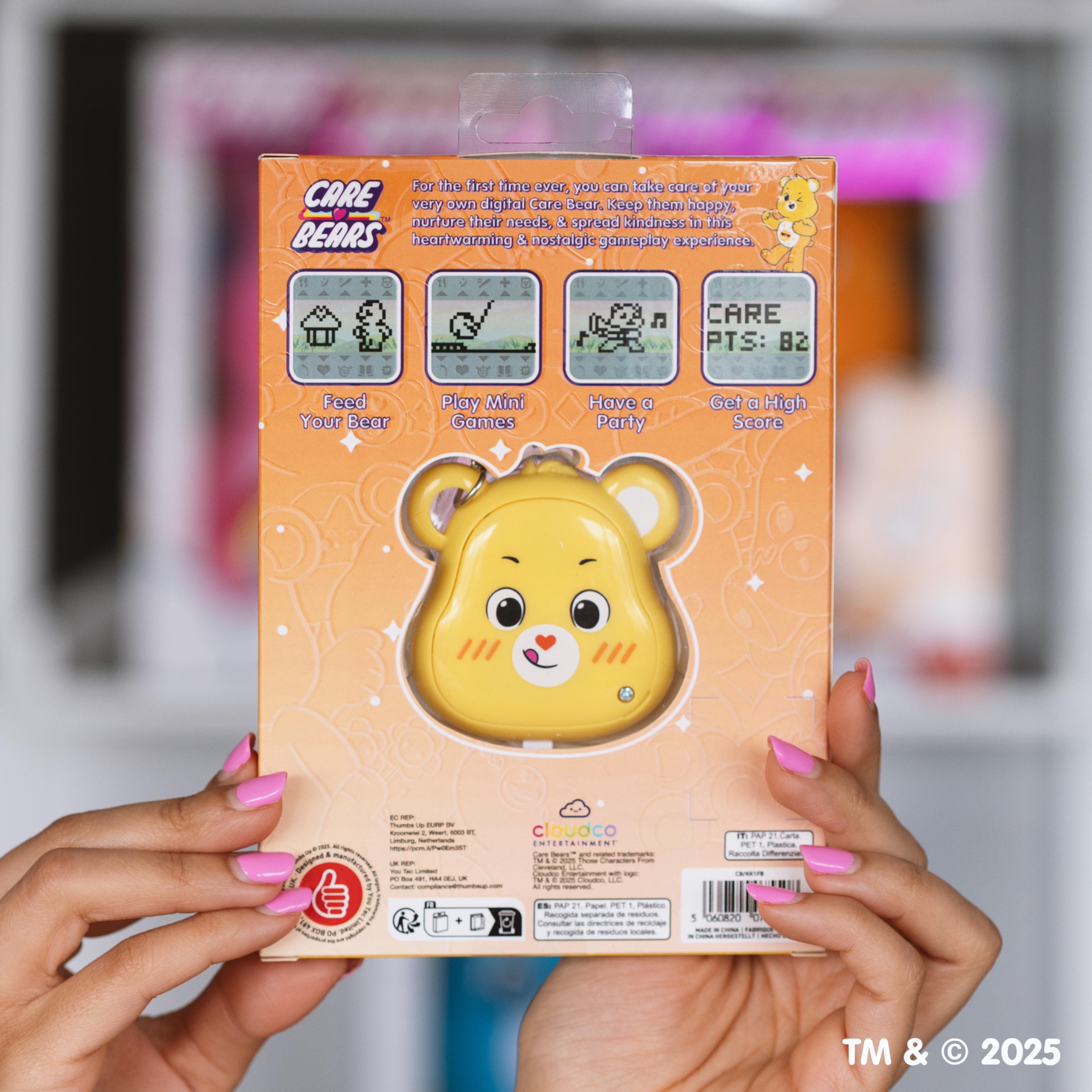 Een persoon houdt een Care Bears-speelgoeddoos vast. Het is geel met een spel in de vorm van een beer. De doos heeft speliconen en tekst.