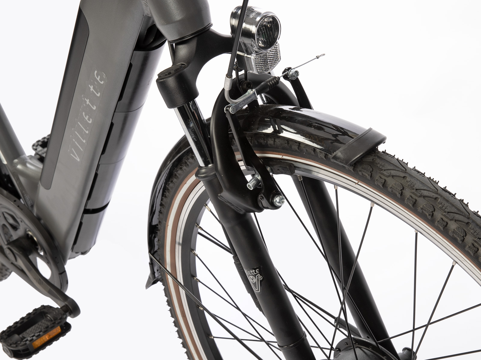 Close-up van een voorwiel van een fiets. Het frame is grijs, de band is zwart. De koplamp is zichtbaar, evenals de voorvork.