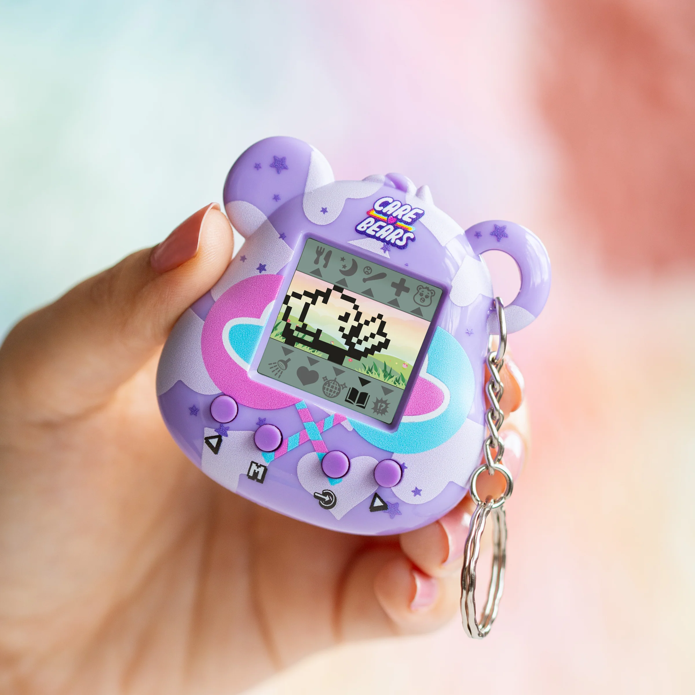 Een persoon houdt een paarse Care Bears digitale huisdier vast. Het heeft een scherm met een gepixeleerde beer en pictogrammen, met een sleutelhanger.