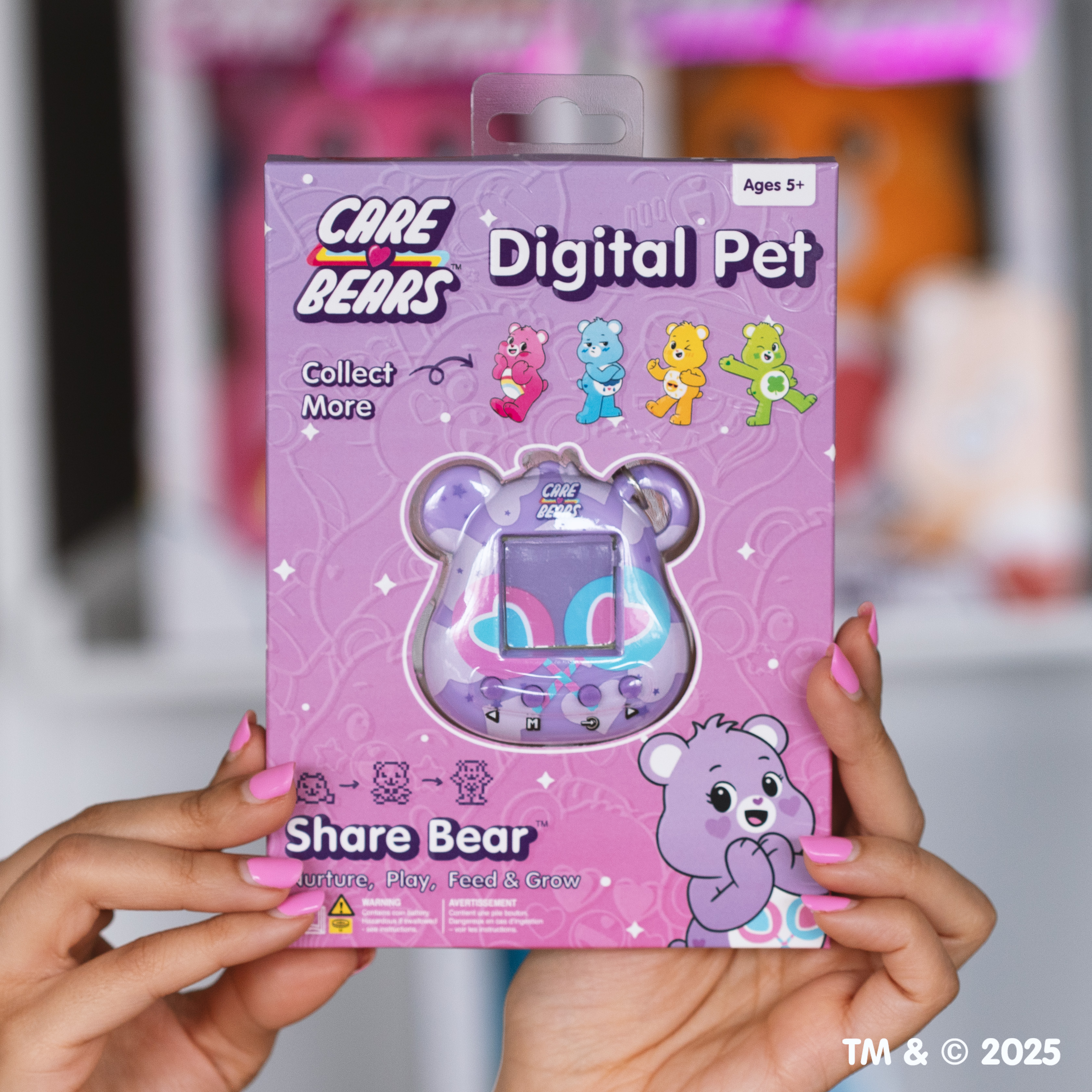 Handen houden een Care Bears Digital Pet doos vast. De doos is roze en paars met Care Bears-personages en een digitaal huisdier-speeltje.