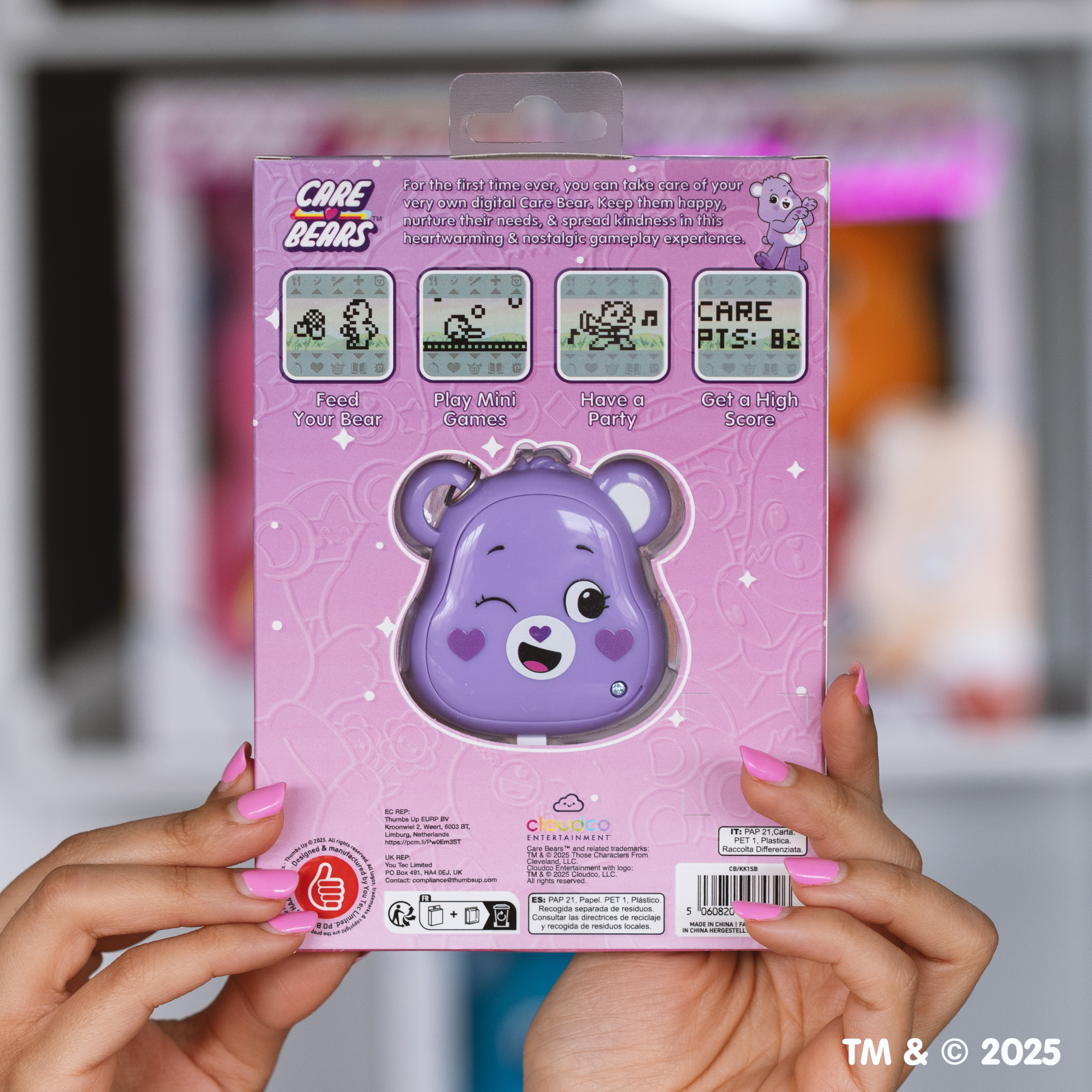 Een persoon houdt een digitale speelgoeddoos van Care Bears vast. De doos toont een paars berenspeelgoed. Roze nagels zijn zichtbaar.