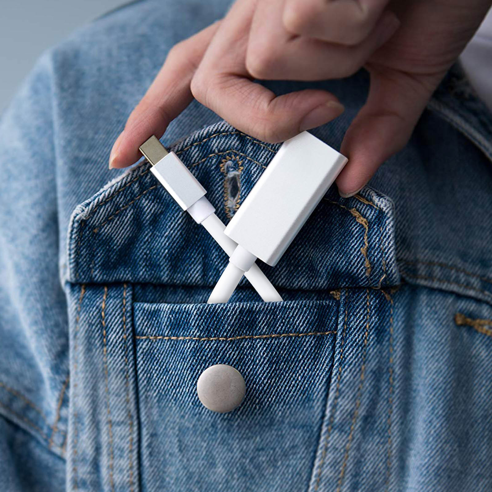 Una mano tiene un adattatore e un cavo USB-C bianchi sopra una tasca di una giacca di jeans. L'adattatore è parzialmente nella tasca.