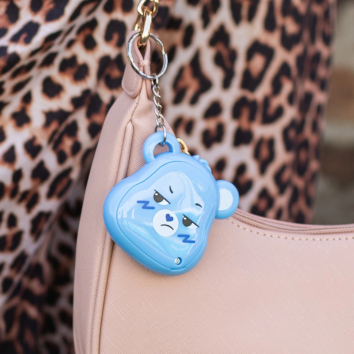 Een blauwe Care Bear-sleutelhanger hangt aan een roze tas. Luipaardprintstof op de achtergrond.