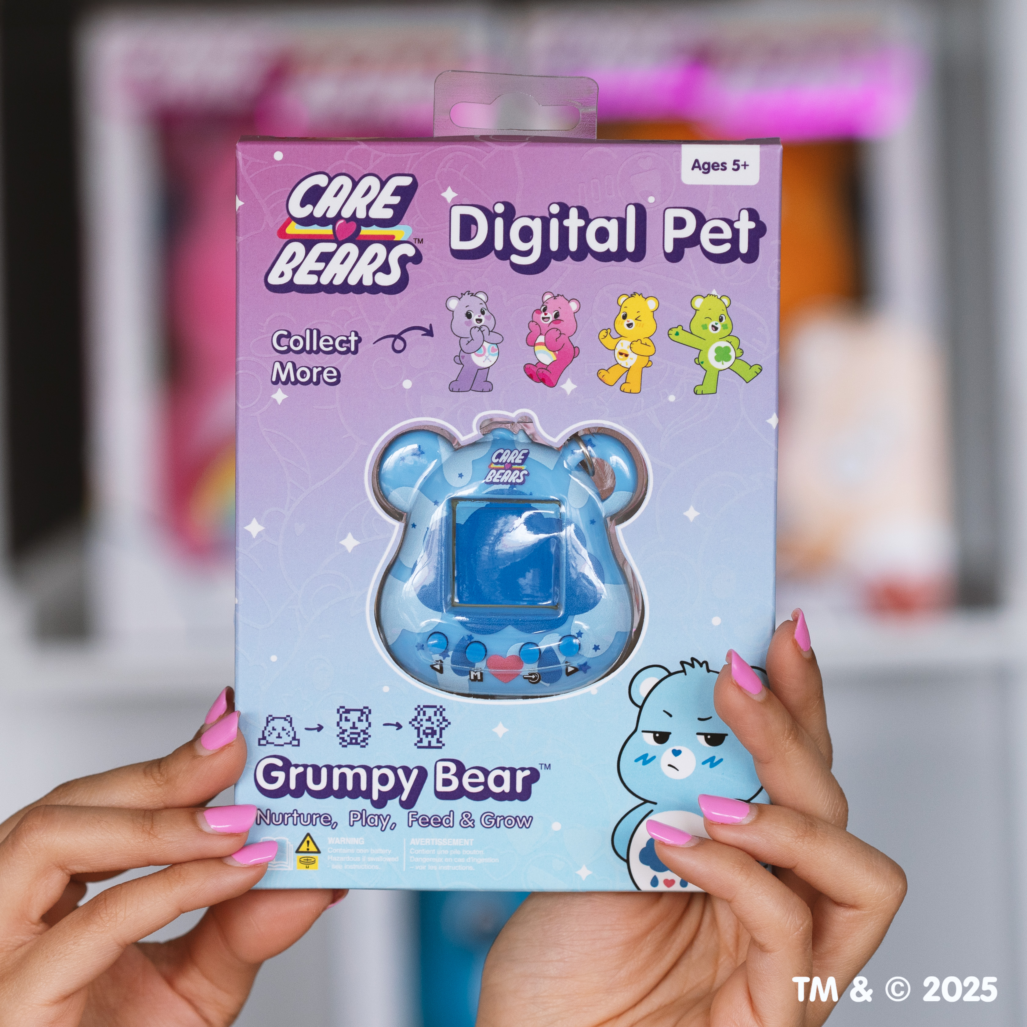 Handen houden een Care Bears Digital Pet doos vast met Grumpy Bear. De doos is blauw, met zichtbaar scherm.