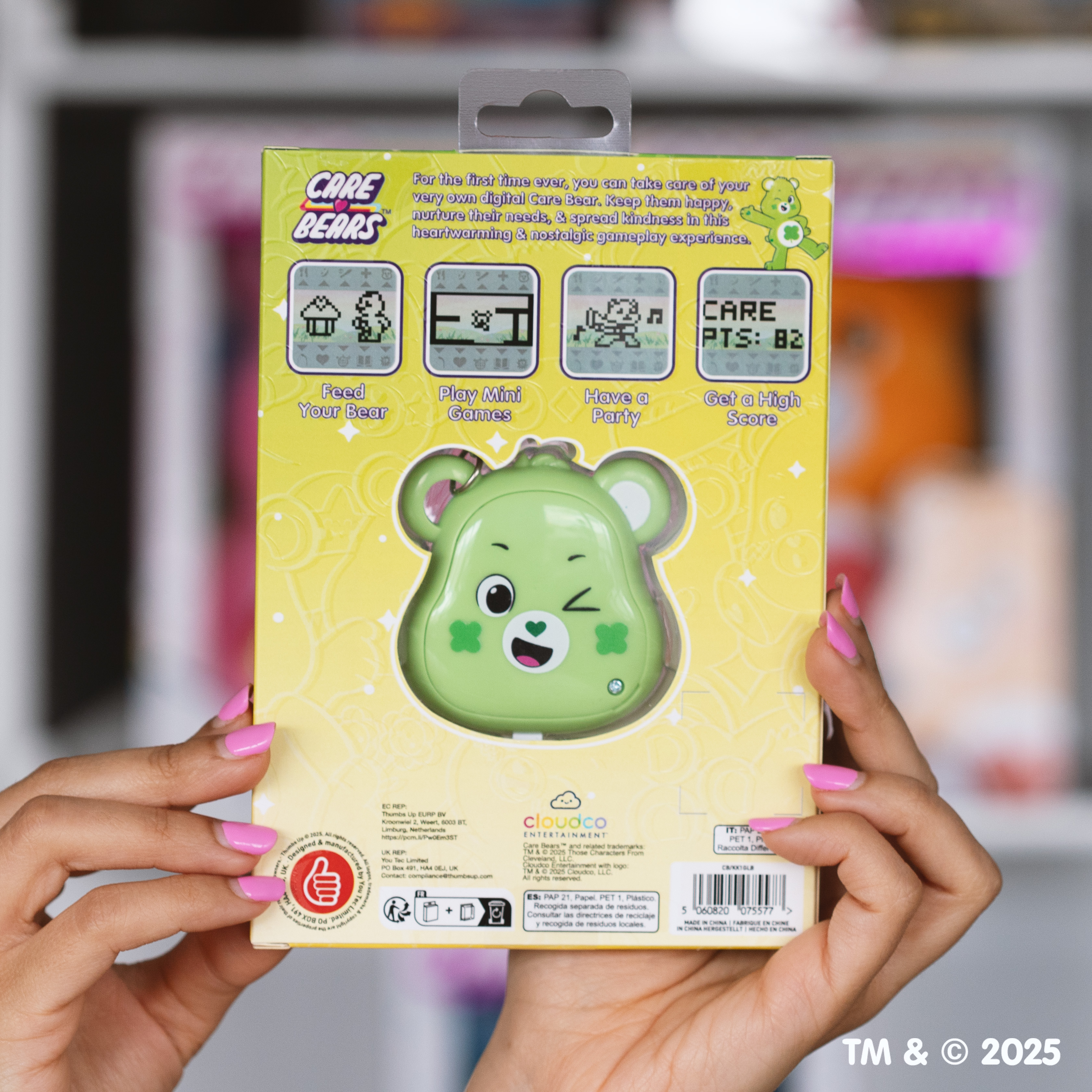 Een persoon houdt een Care Bears digitale speelgoeddoos vast. Het heeft een groene beer met een knipoog. De achtergrond is lichtroze.