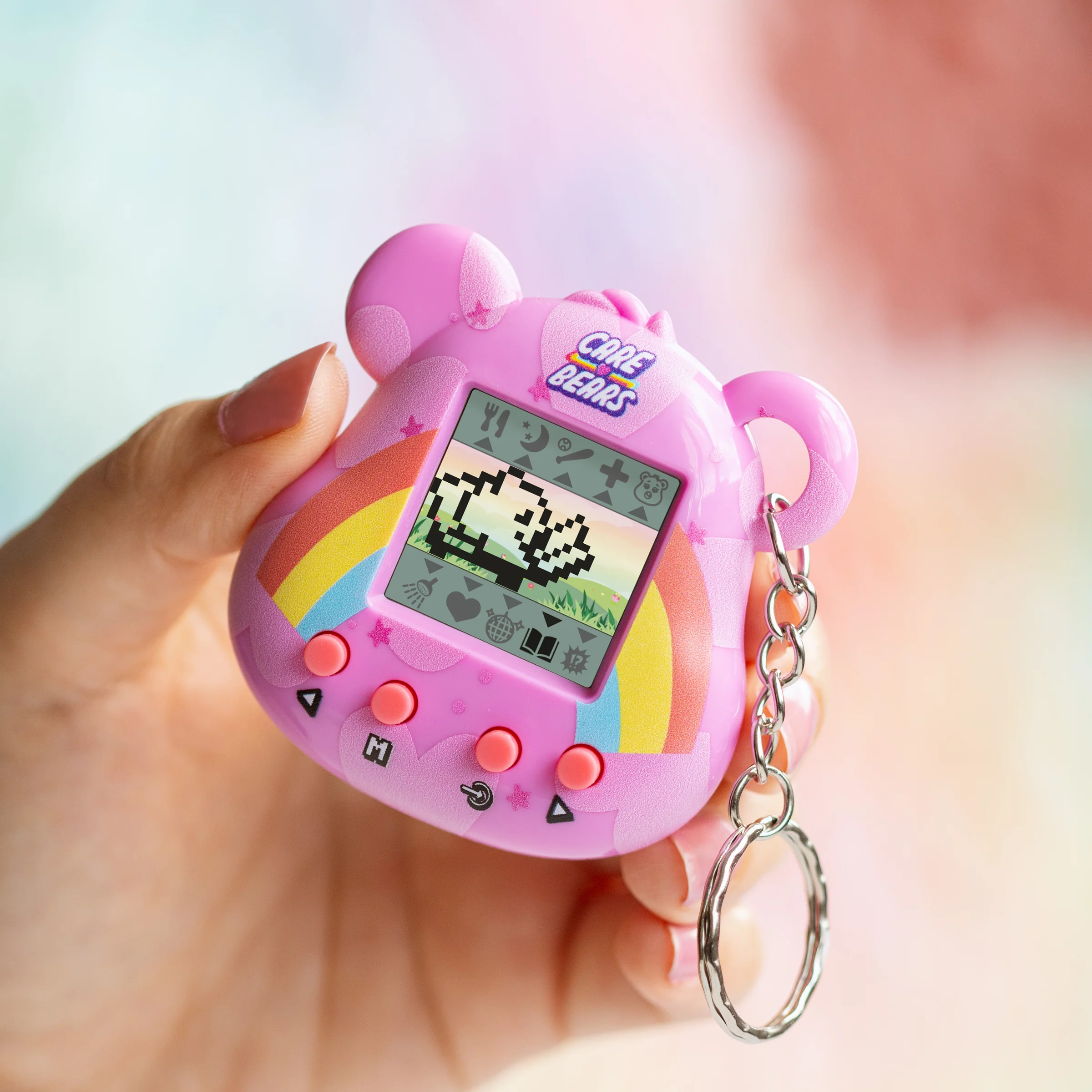 Een roze Care Bears Tamagotchi wordt door een hand vastgehouden. Het heeft een scherm met een gepixeleerde beer en regenboogontwerp.