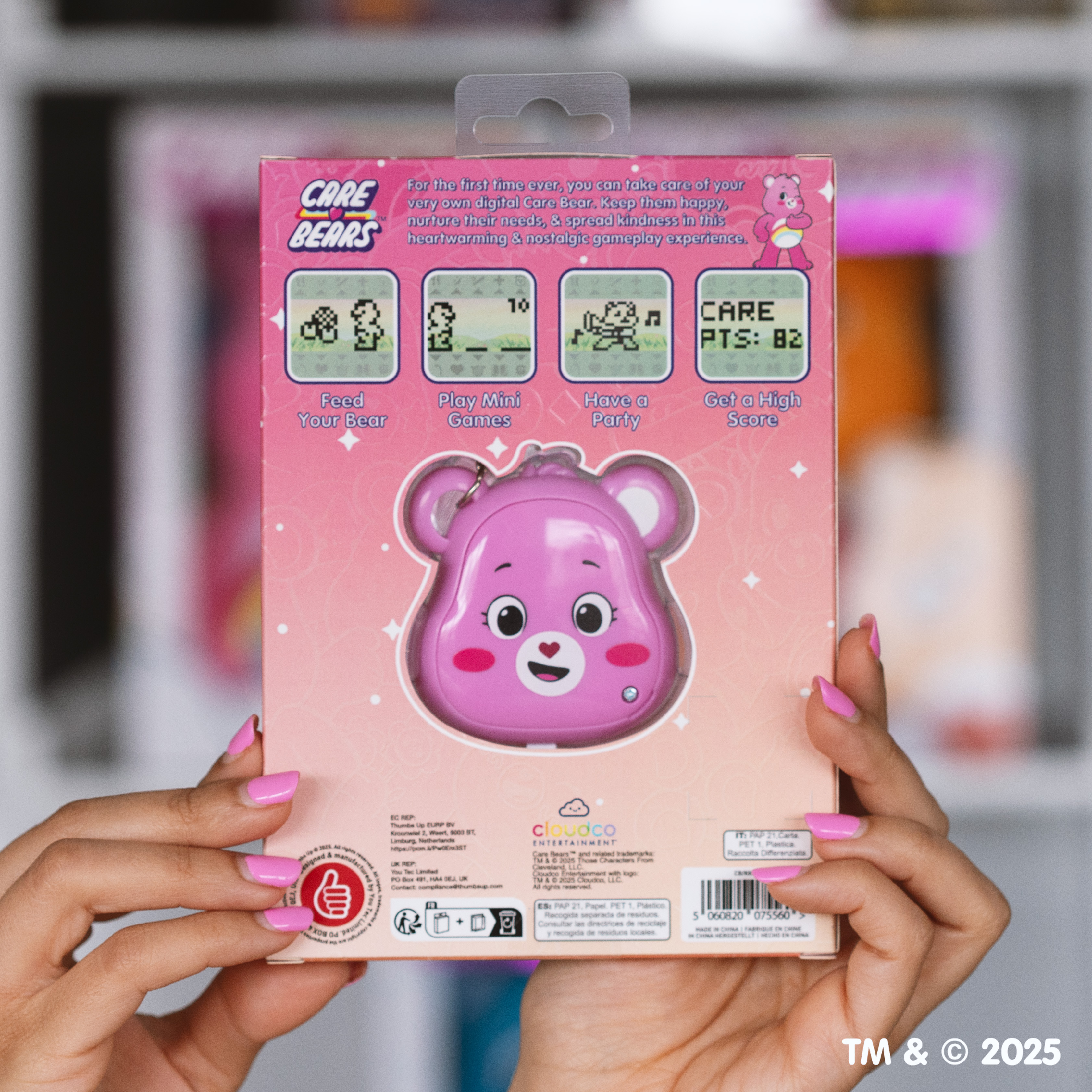 Handen houden een roze Care Bears speelgoedverpakking vast. De verpakking toont een roze beer-vormig digitaal speelgoed.