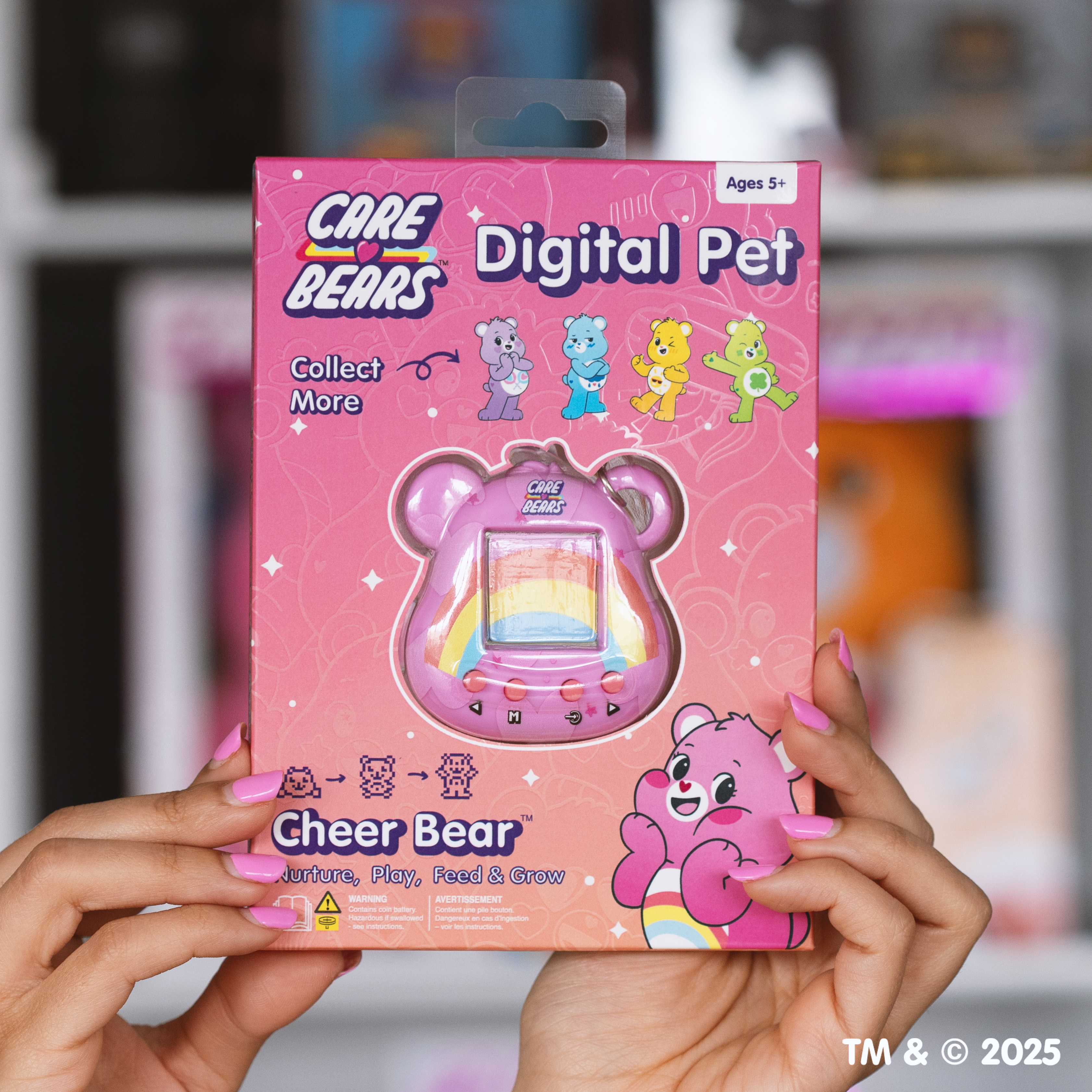 Een persoon houdt een roze Care Bears Digital Pet-doos vast. De doos heeft een digitaal huisdier, het ontwerp bevat beren en regenbogen.