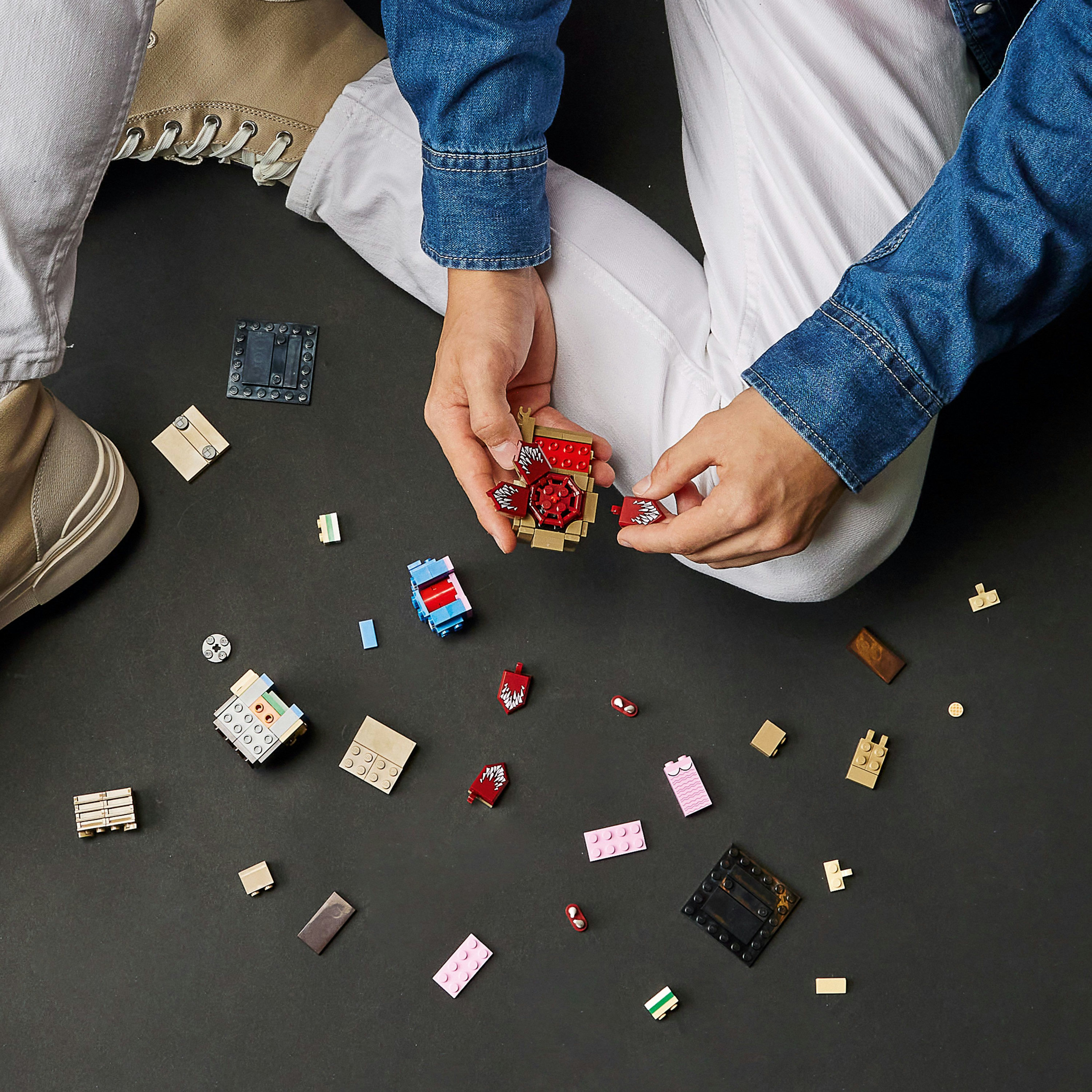 Persoon zittend met Lego-stukken op een zwart oppervlak. Ze zijn een Lego-model aan het in elkaar zetten, met diverse verspreide onderdelen.