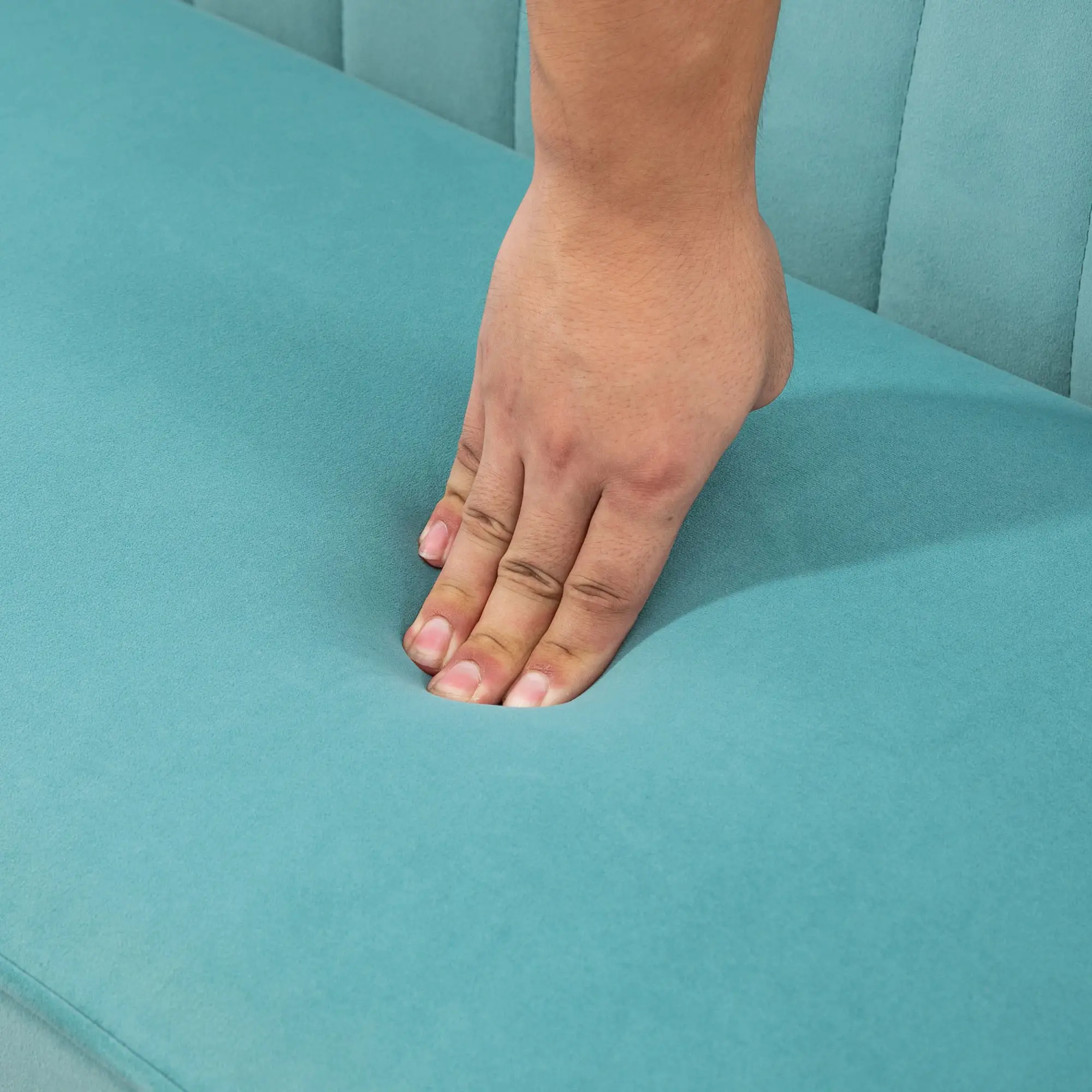 Eine Hand drückt auf ein türkisfarbenes Kissen. Die Hand ist braun und das Kissen Teil eines größeren Sitzes.