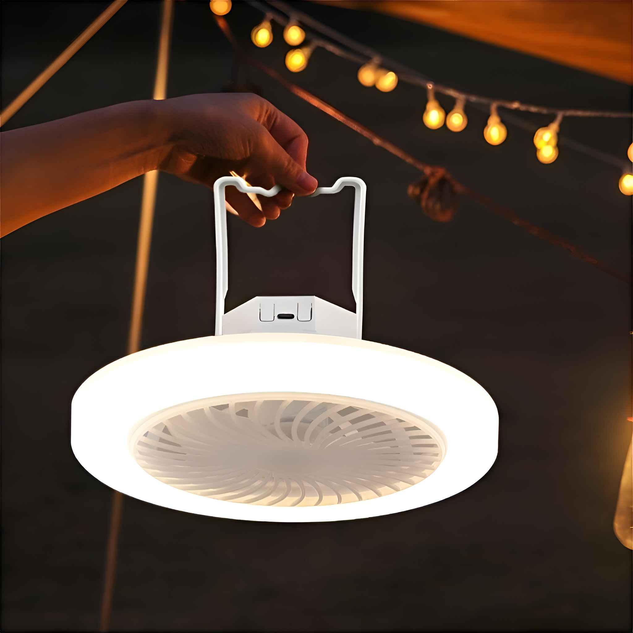 Eine Hand hält eine weiße Campinglaterne mit Ventilator. Die Laterne ist beleuchtet, im Hintergrund eine Lichterkette.