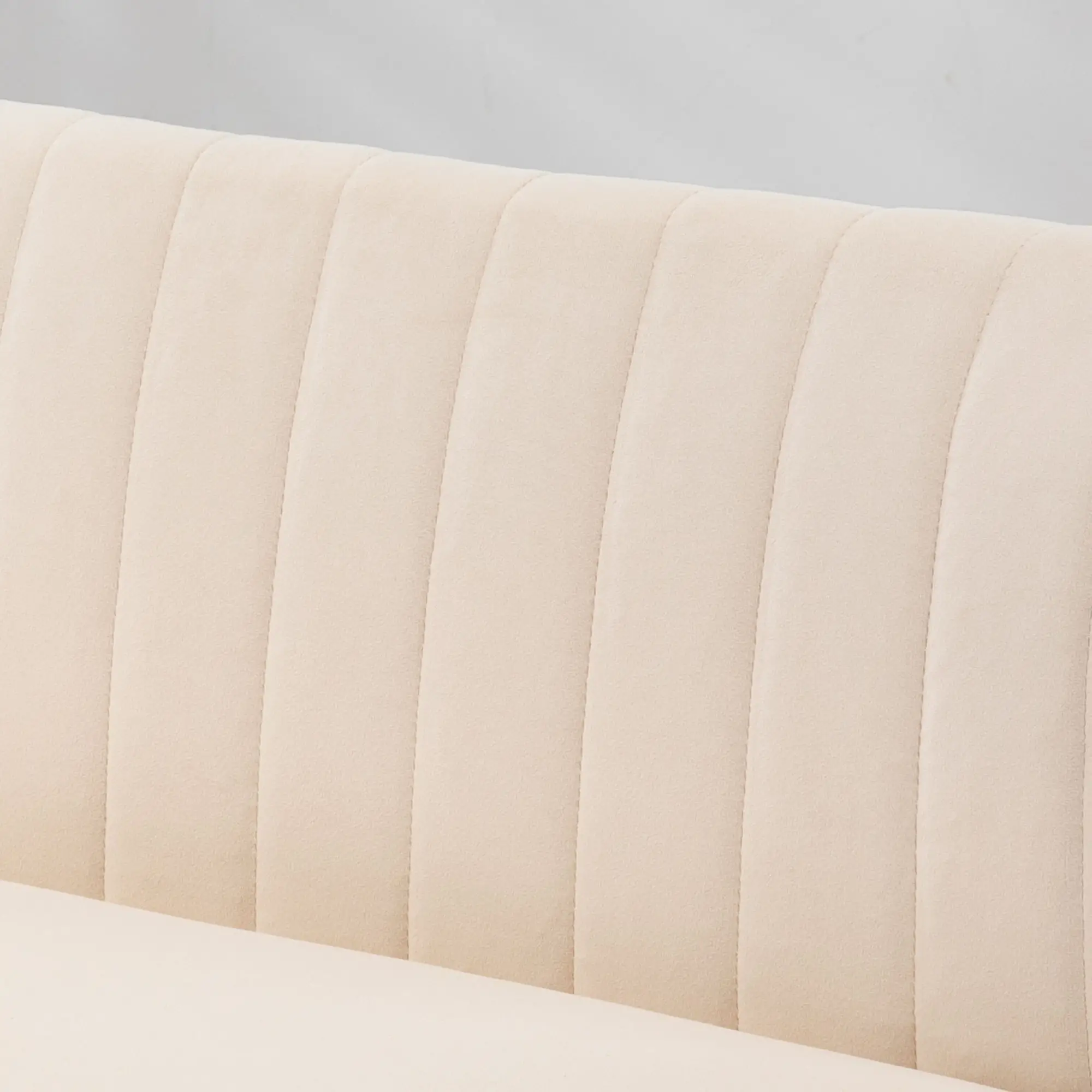 Nahaufnahme einer beige, vertikal gerippten gepolsterten Oberfläche, wahrscheinlich eine Sofarückenlehne, vor einem neutralen, hellfarbigen Hintergrund.