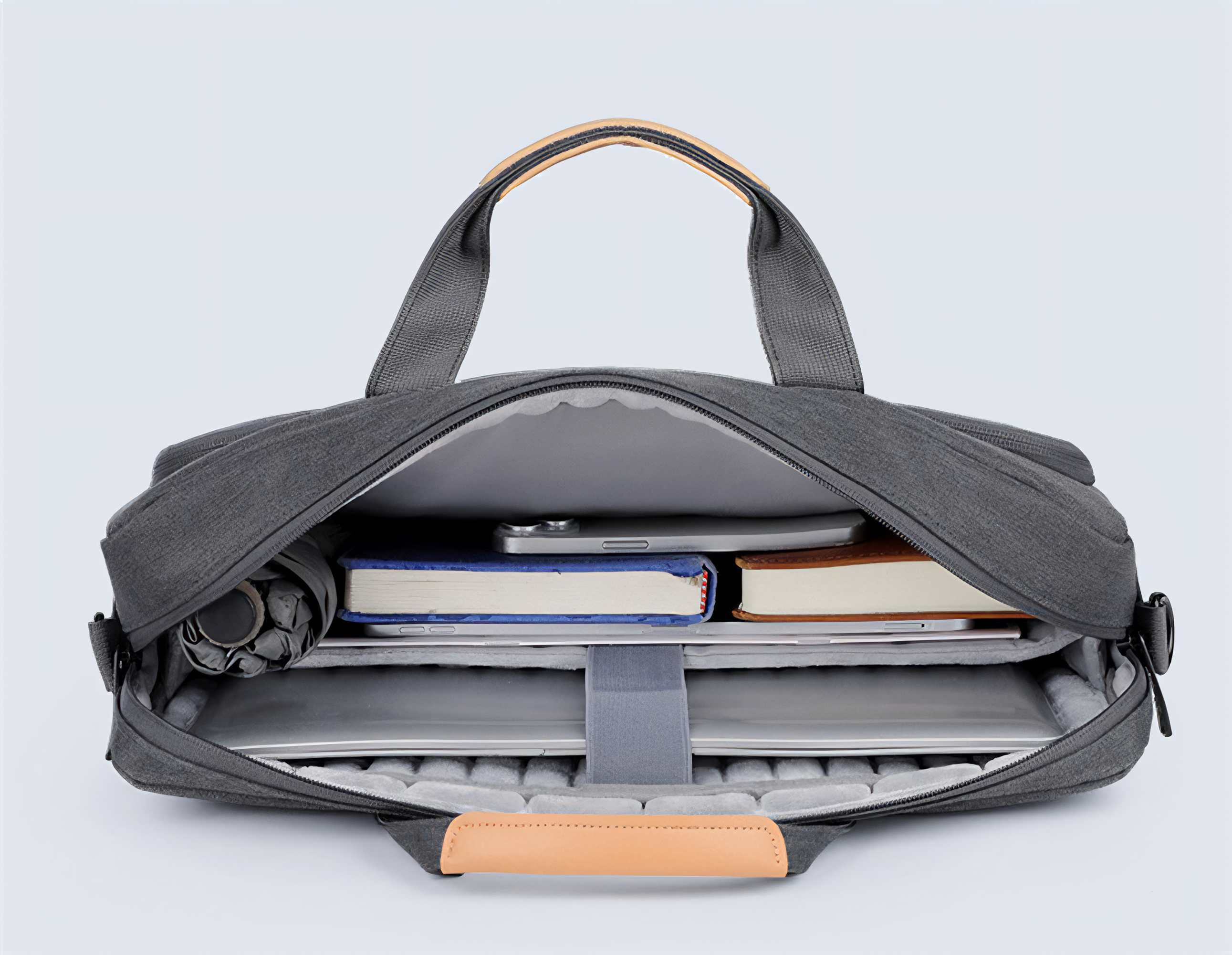 Geöffnete graue Laptoptasche mit Büchern, Regenschirm und Laptop. Hellbraune Griffe. Hellgrauer Innenraum. Weißer Hintergrund.