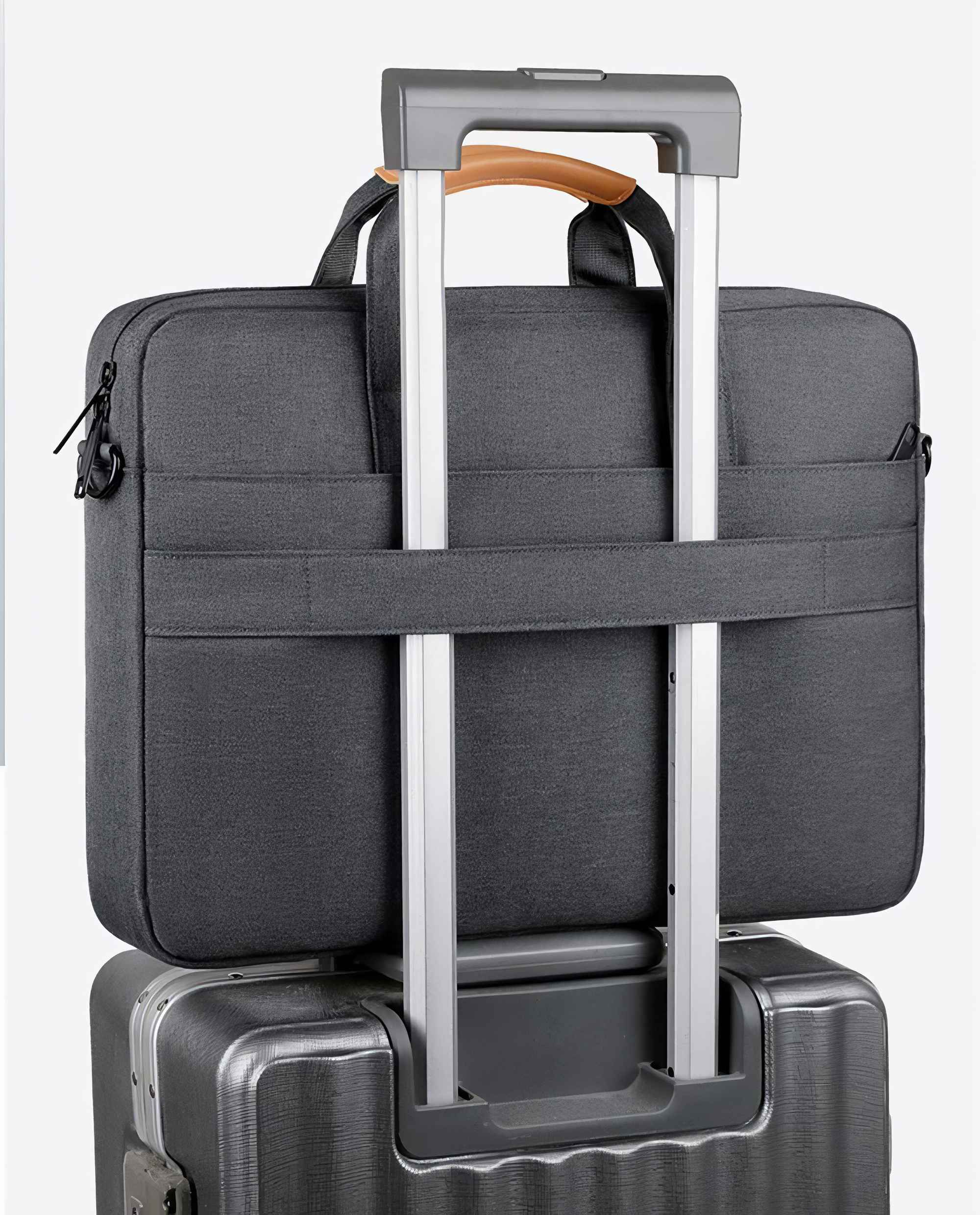 Eine graue Laptoptasche liegt auf einem grauen Koffer. Die Tasche hat einen Griff mit braunem Leder. Der Koffer hat einen silbernen Griff.