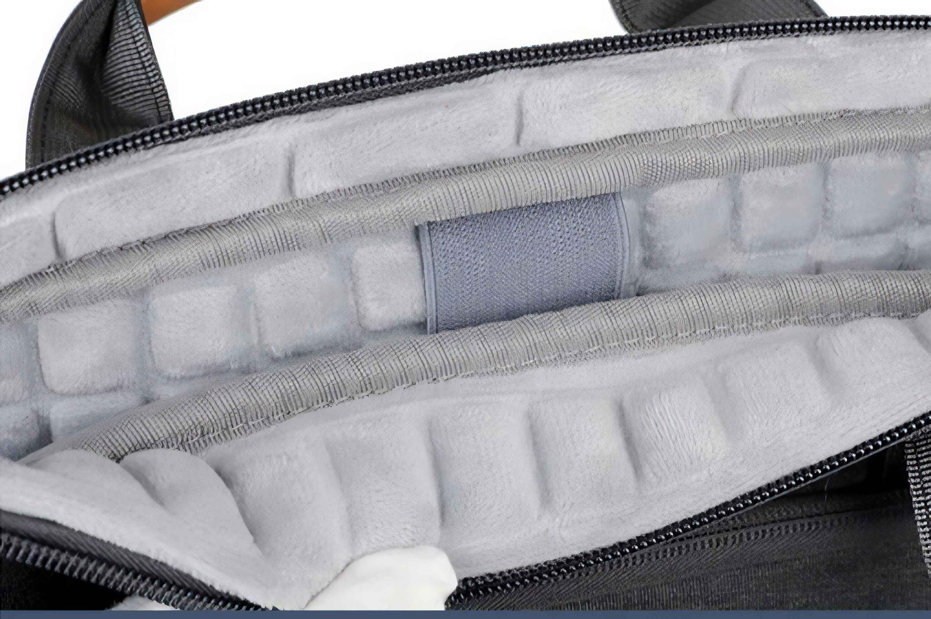 Offenes Laptop-Tascheninnere. Graue, gepolsterte Abschnitte sichtbar, mit einem grauen Riemen in der Mitte. Schwarzer Reißverschluss oben und unten.